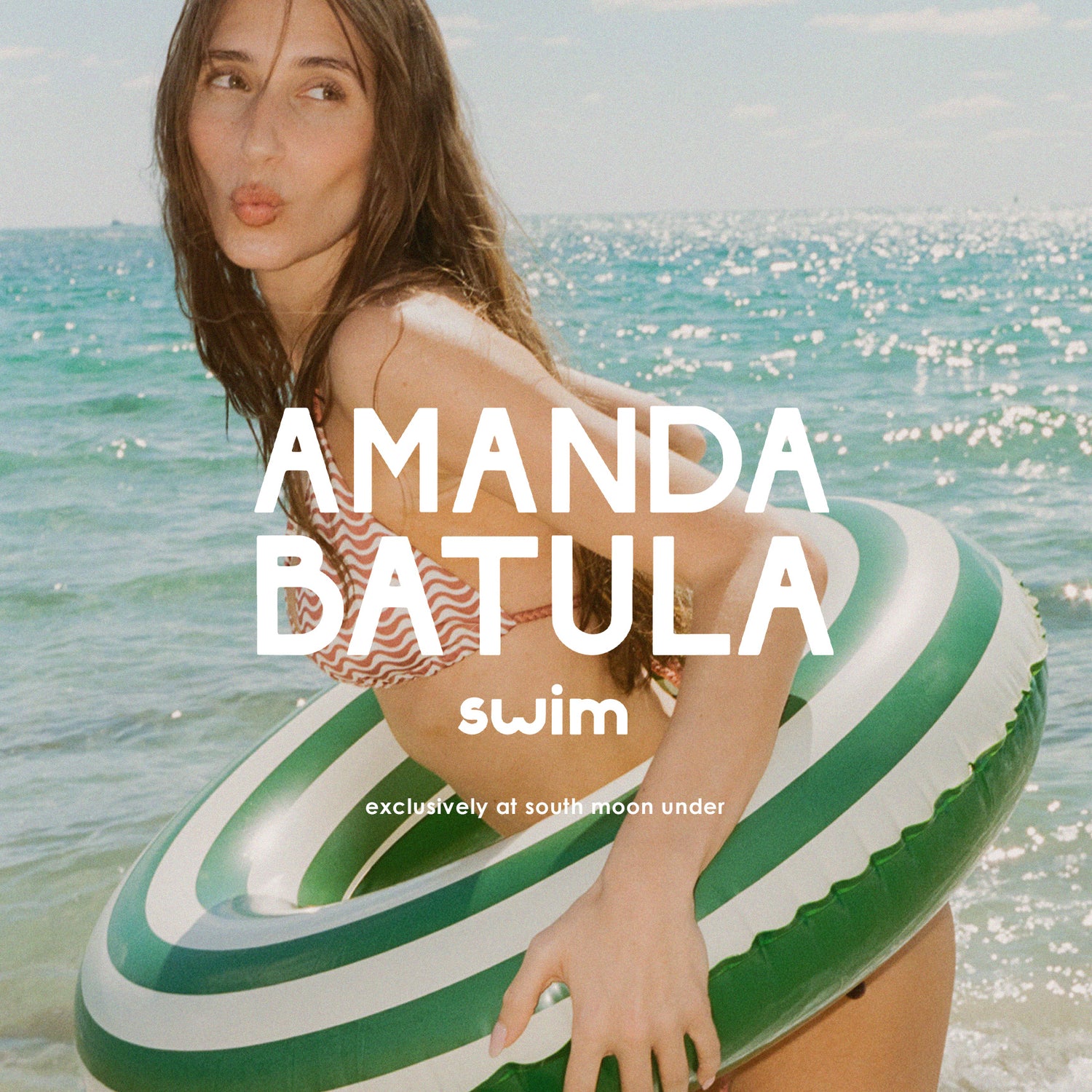 Woman on a striped inner tube with 'Amanda Batula swim' branding at the beach.