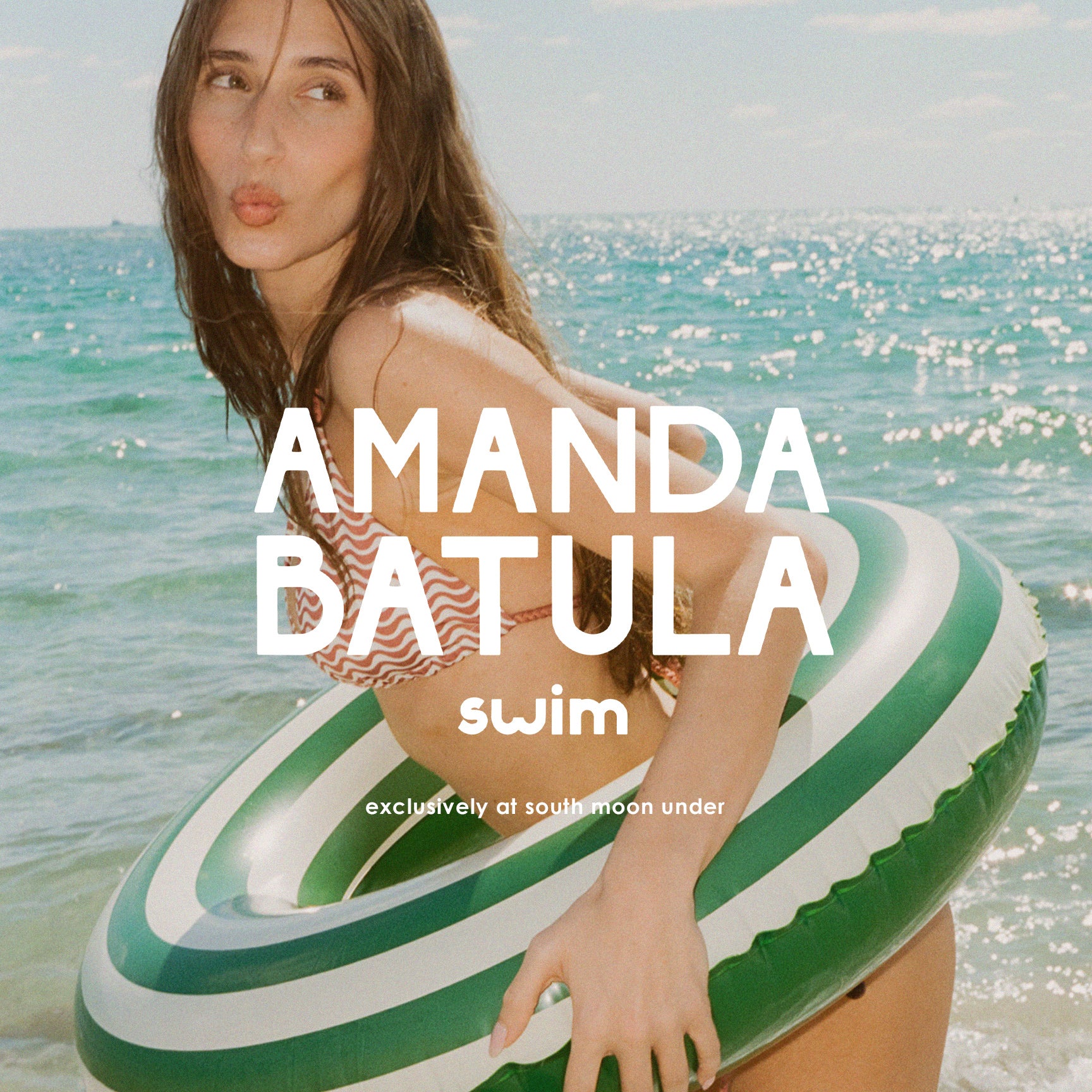 Woman on a striped inner tube with 'Amanda Batula swim' branding at the beach.