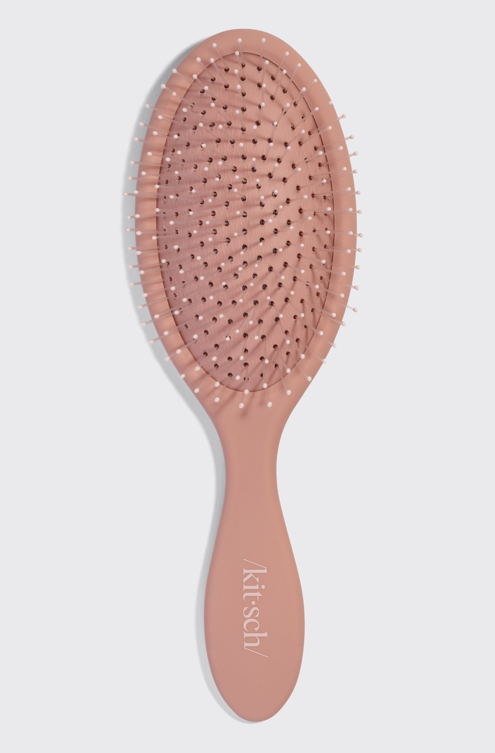 The Kitsch Wet/dry Brush features a pink, curved handle and flexible, white-tipped bristles for easy, frizz-free styling. The brand name “Kitsch” is printed in white on the handle.