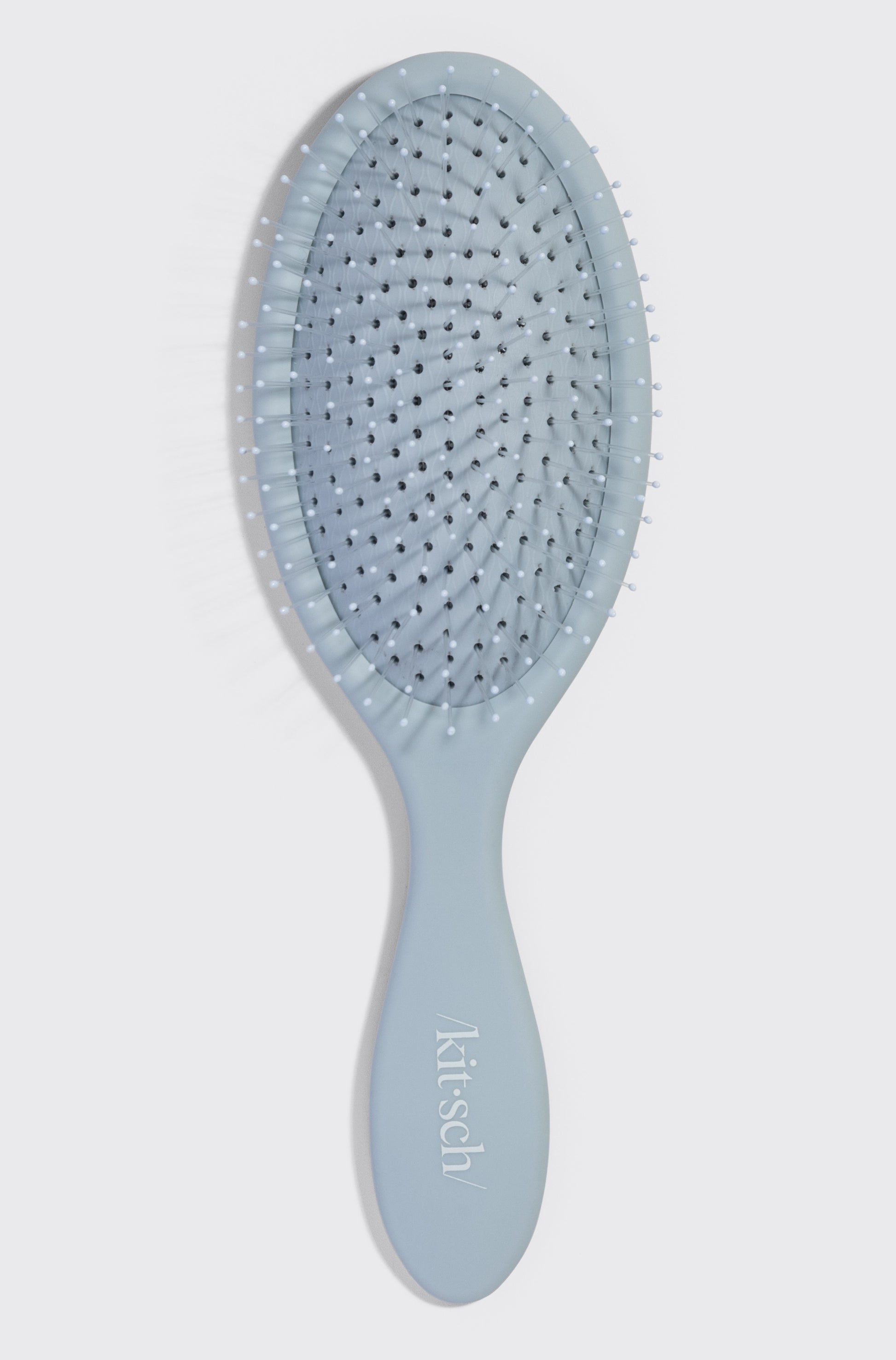 The Kitsch Wet/Dry Brush, in light blue with soft bristles and an oval paddle, is shown on a white background. Ideal for detangling and achieving frizz-free hair, it's suitable for all hair types. Brand name appears on the handle.