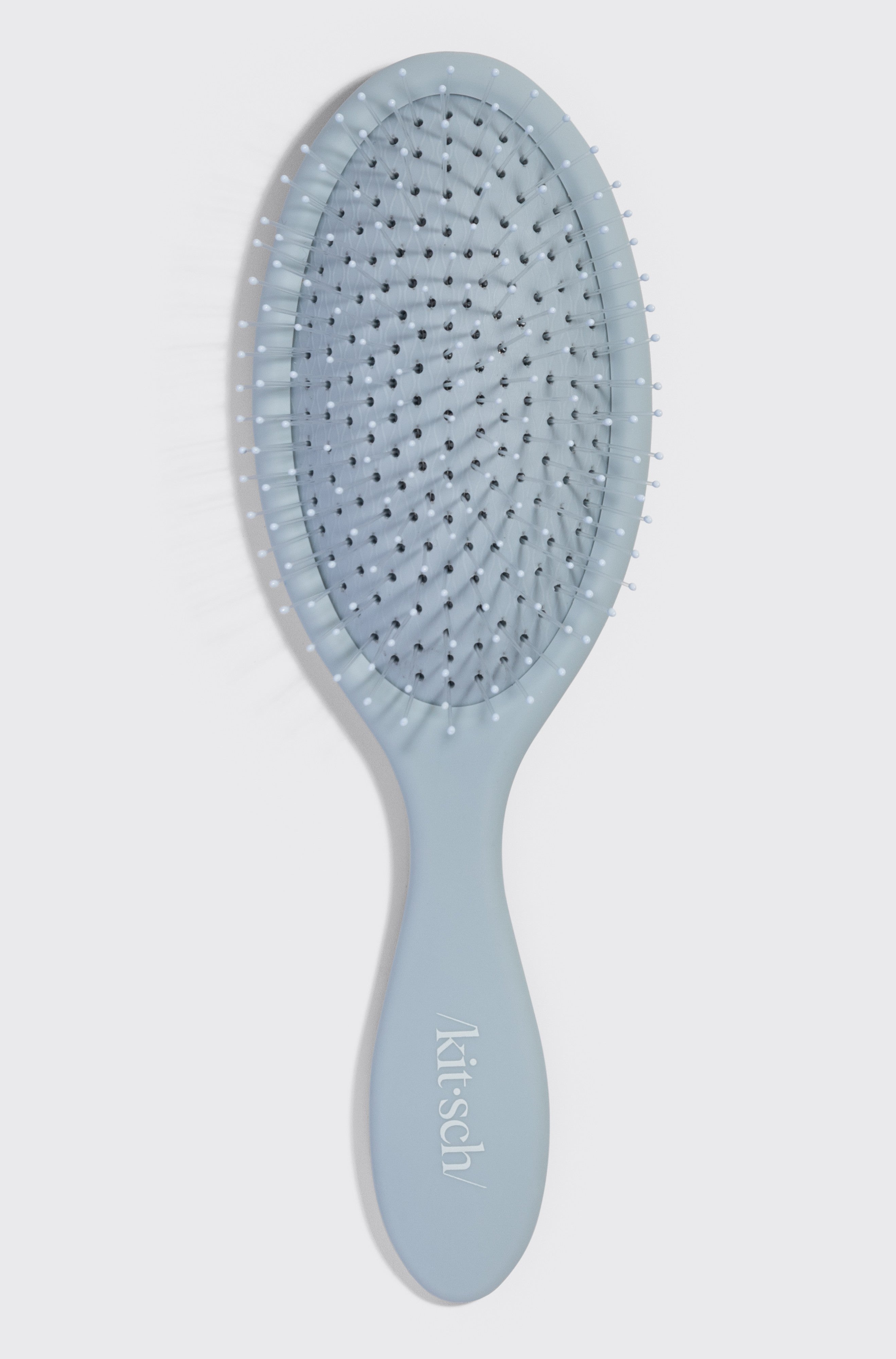 The Kitsch Wet/Dry Brush, in light blue with soft bristles and an oval paddle, is shown on a white background. Ideal for detangling and achieving frizz-free hair, it's suitable for all hair types. Brand name appears on the handle.
