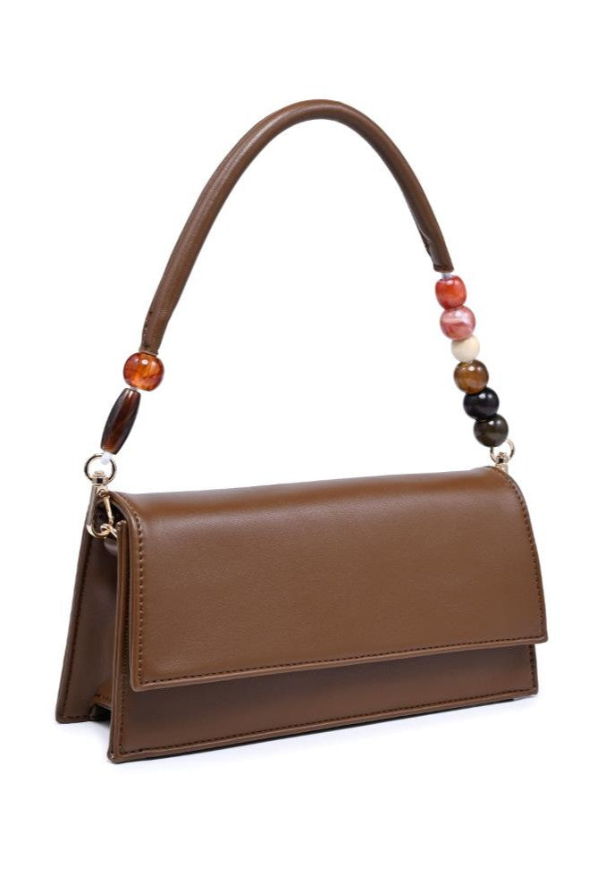The Brooks Shoulder Bag by Urban Expressions is a structured black vegan leather handbag with a rectangular silhouette, flap closure, padded top handle, and multicolored round beads accenting each side.