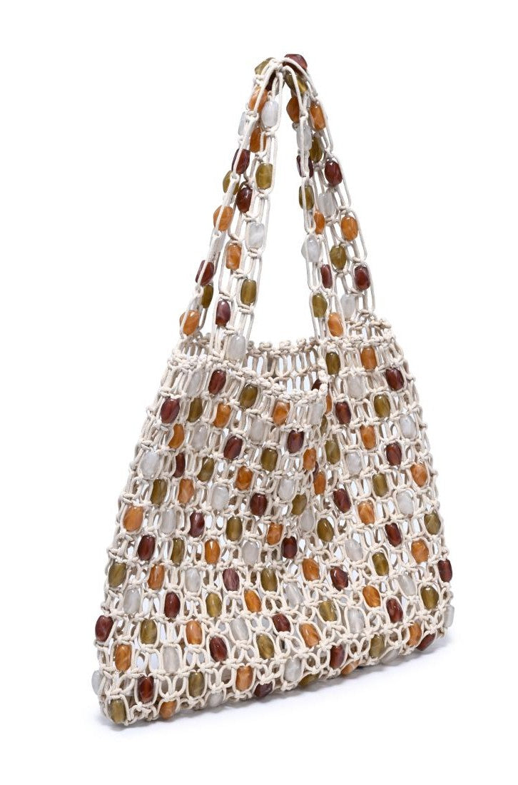 The Asher Beaded Beach Bag by Urban Expressions is a cream macramé tote with white, amber, and brown square beads and two handles, offering a chic boho style for any occasion.