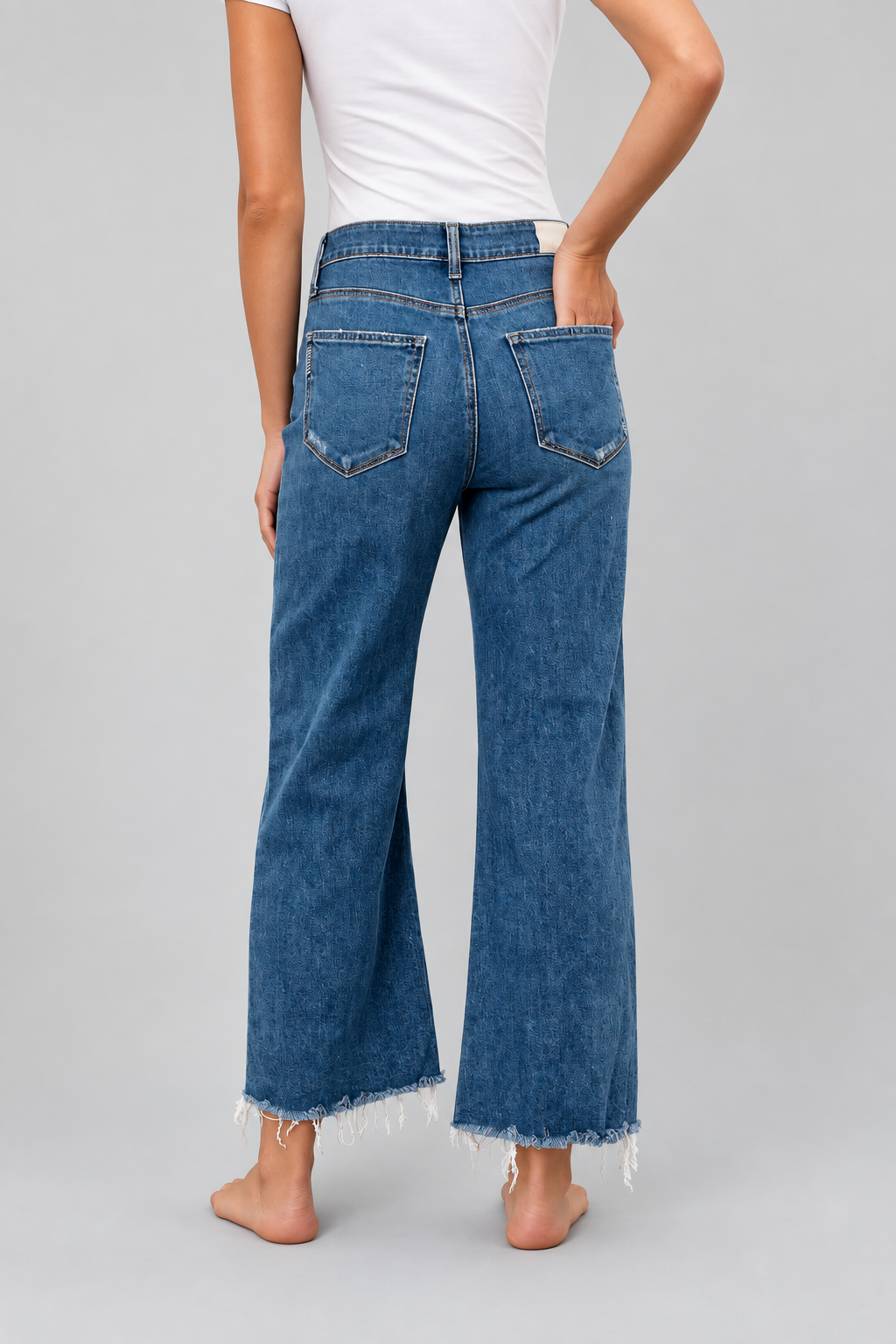 Woman wearing blue denim jeans with raw frayed hems and white t-shirt, back view.