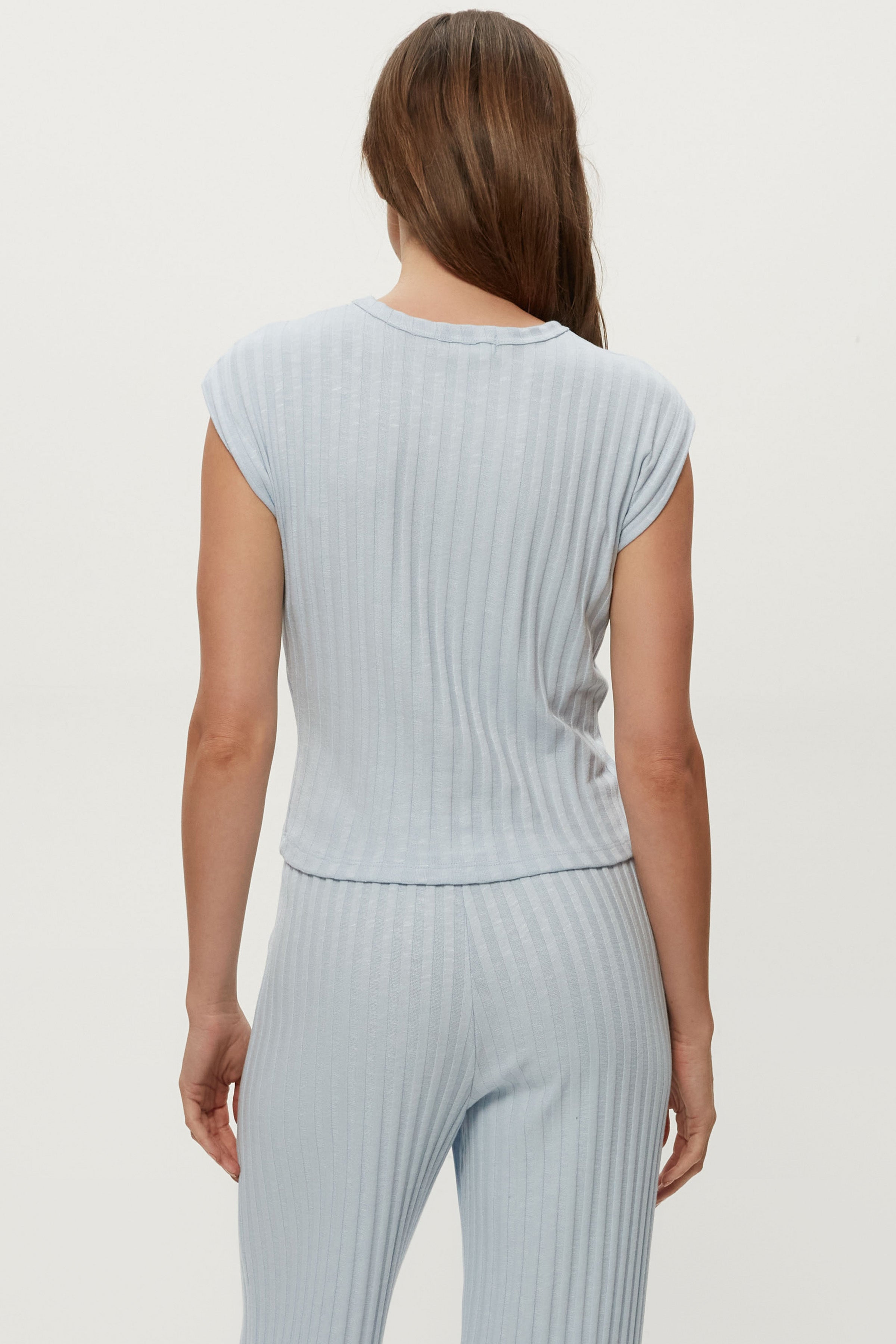 A woman with long brown hair is seen from behind wearing the Michael Stars Jinny Power Shoulder Top in light blue, paired with matching ribbed pants, creating a comfortable yet stylish look against a plain light background.