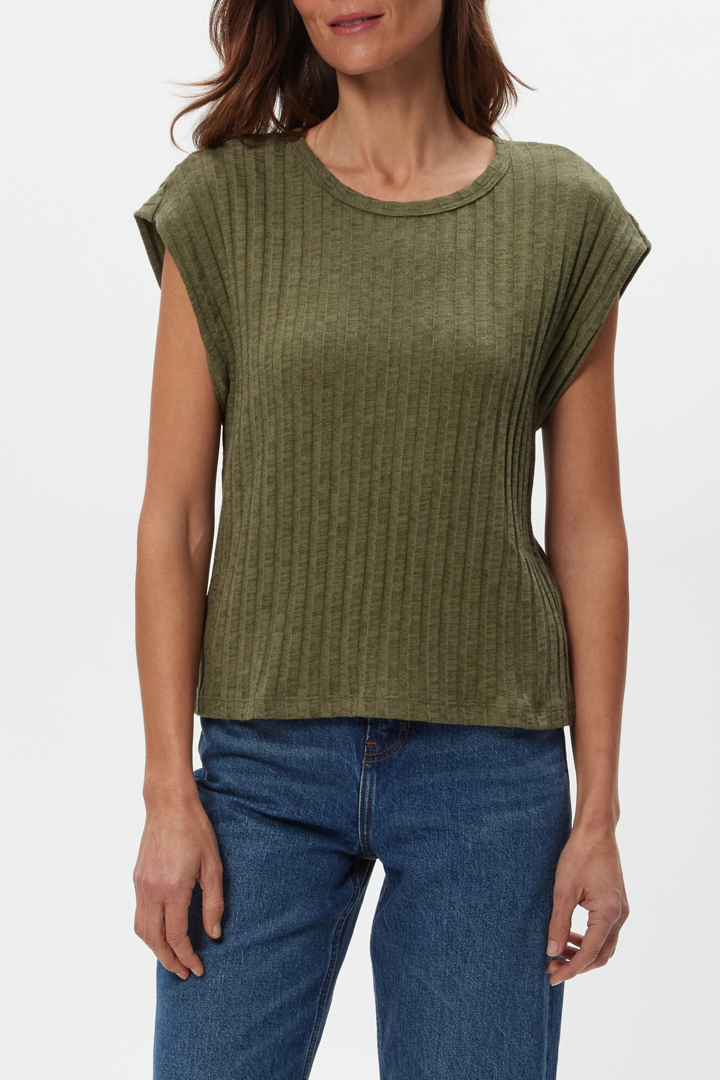 A woman models the Michael Stars Jinny Power Shoulder Top, a fitted ribbed olive green cotton-spandex piece with short sleeves, paired with blue jeans. She stands against a plain white background, her face partially out of frame.