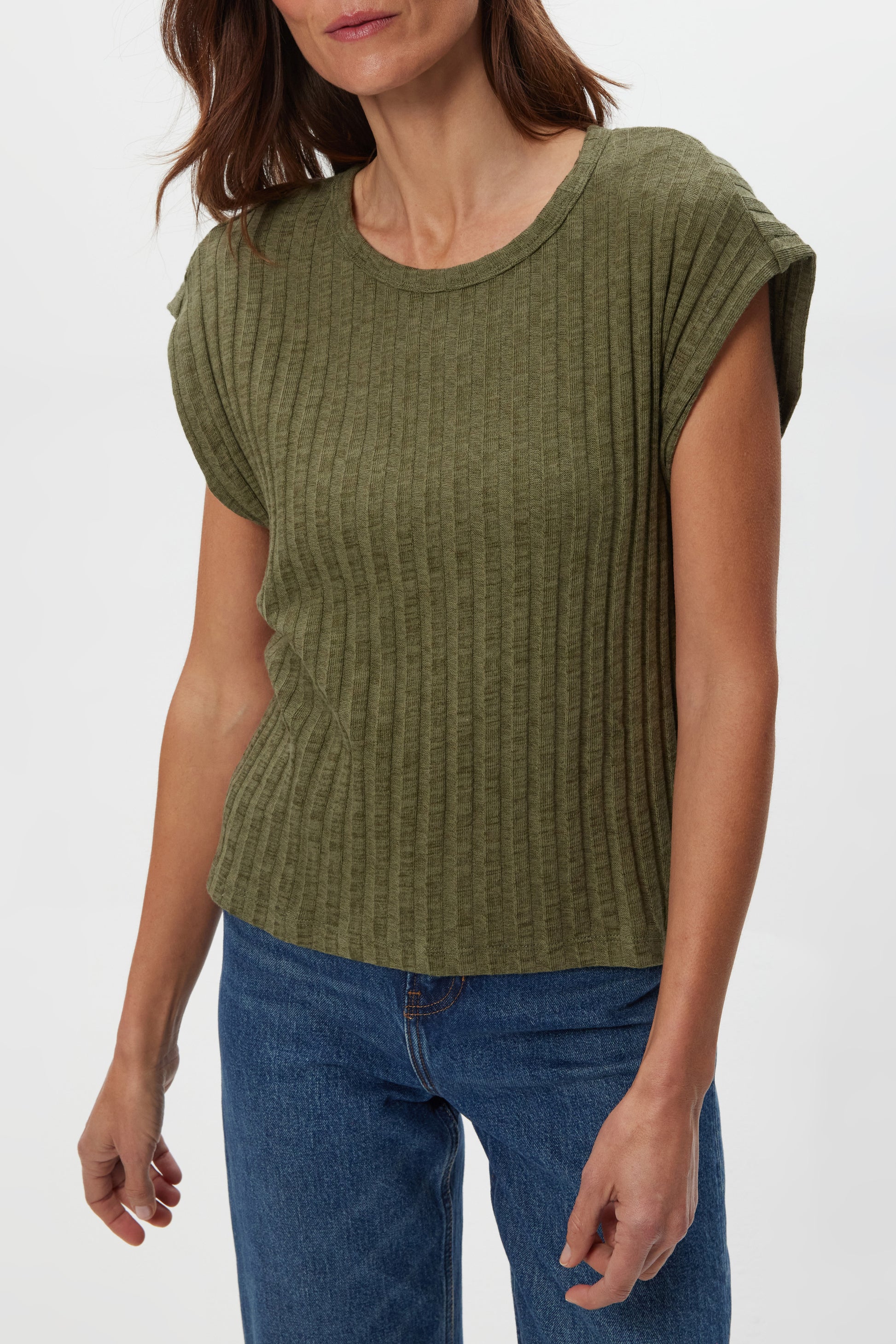 A woman wears the Michael Stars Jinny Power Shoulder Top in olive, paired with blue jeans. The fitted, ribbed top has short sleeves. She stands against a plain white background with her head partly out of the frame.