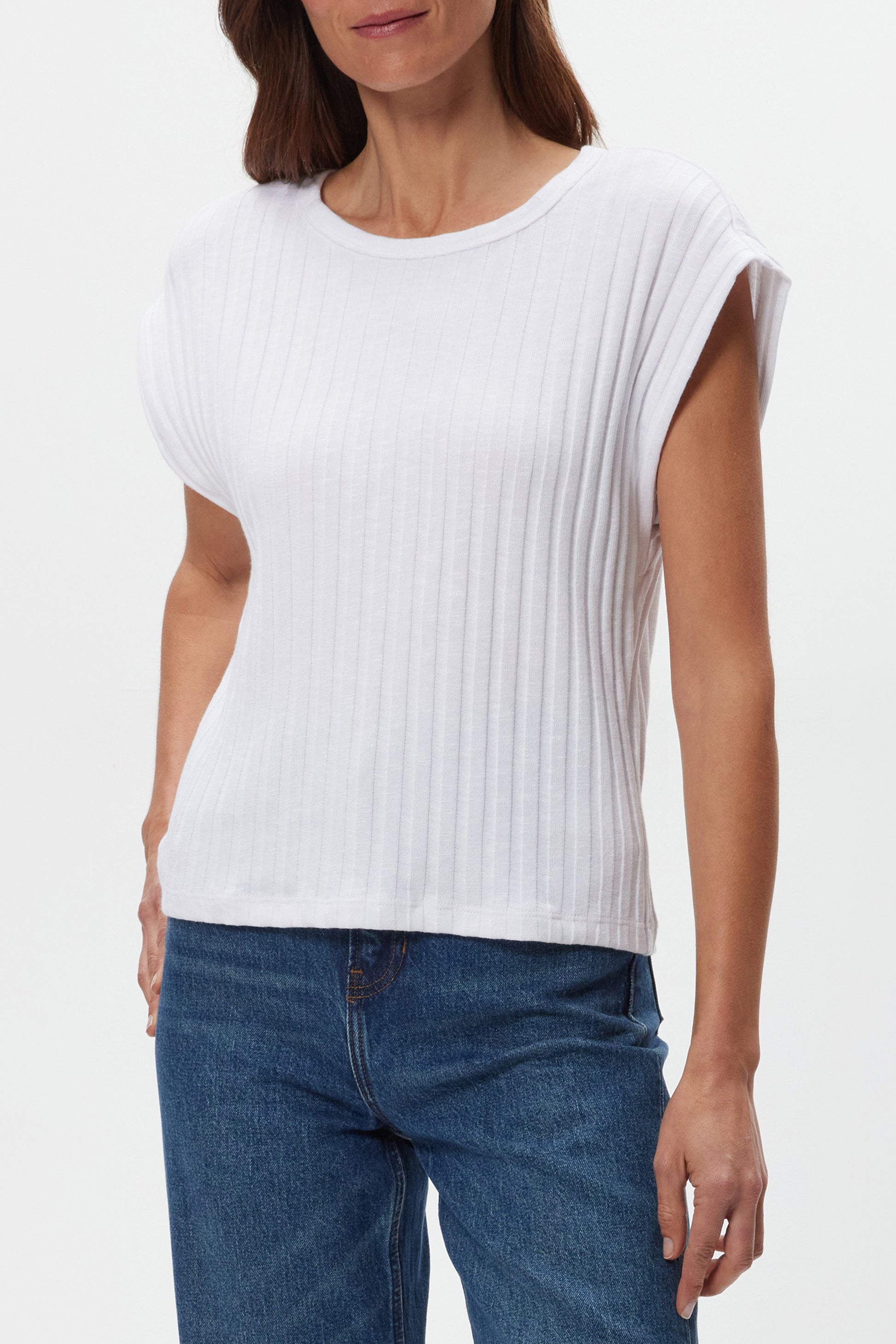 A woman models the Michael Stars Jinny Power Shoulder Top in white, featuring short sleeves and a fitted cotton-spandex blend. She pairs it with blue jeans, standing against a plain white background with her head partially cropped.
