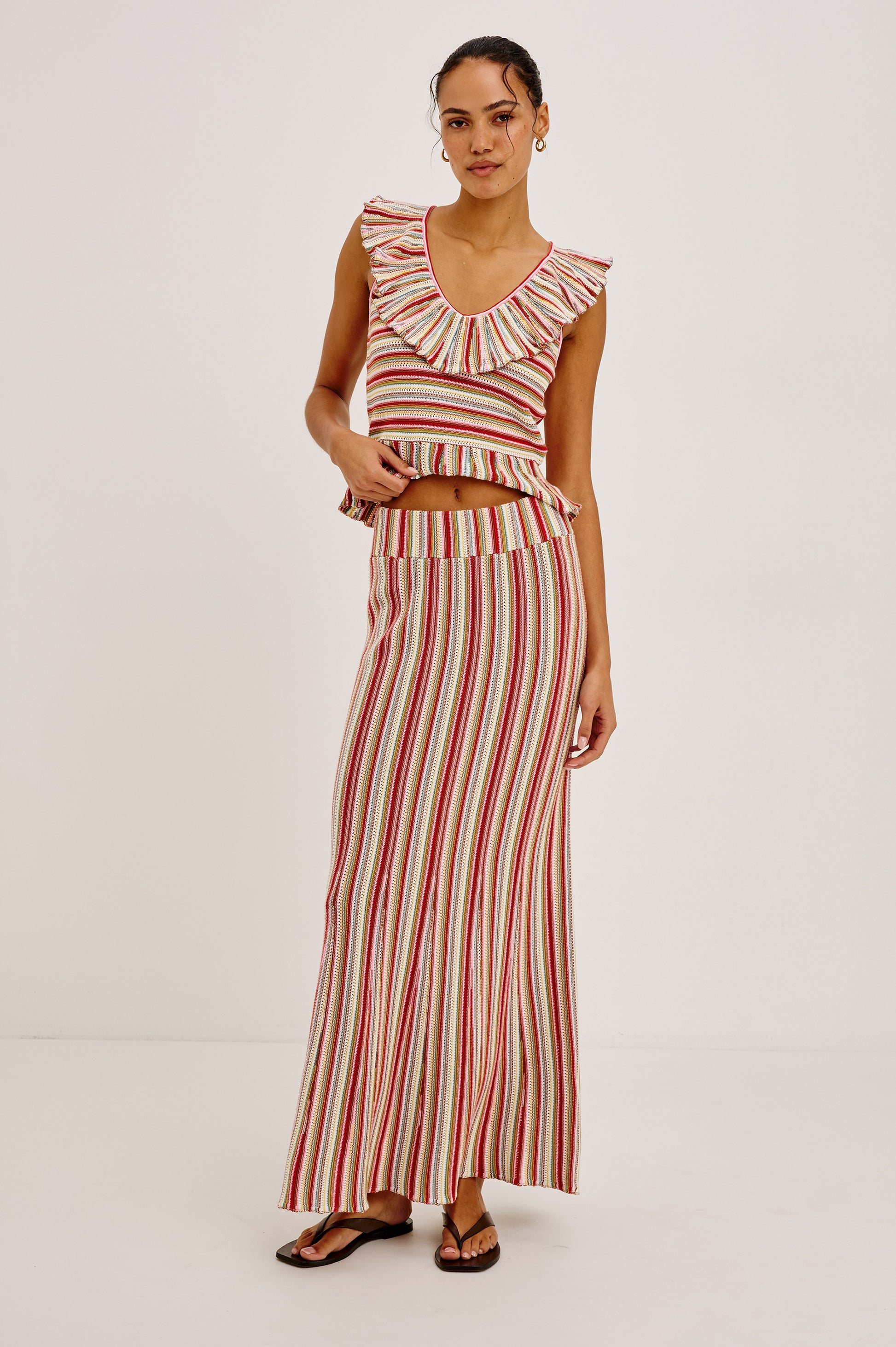 A woman models the Rails Carmelita: a sleeveless, striped two-piece set with a ruffled V-neck crop top and matching long skirt, paired with sandals, standing against a plain white background.