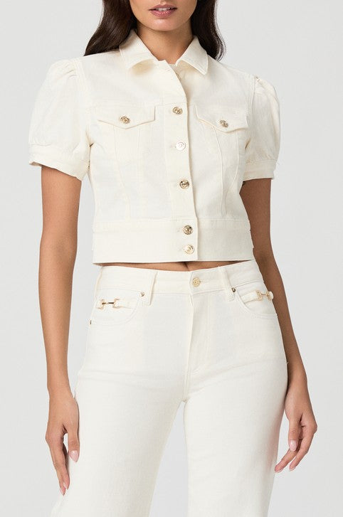 A woman wears the Paige Kendra Denim Jacket in ecru—a short-sleeve, button-up cropped jacket with double chest pockets and puffed sleeves—paired with high-waisted pants; image shown from shoulder to upper thigh.