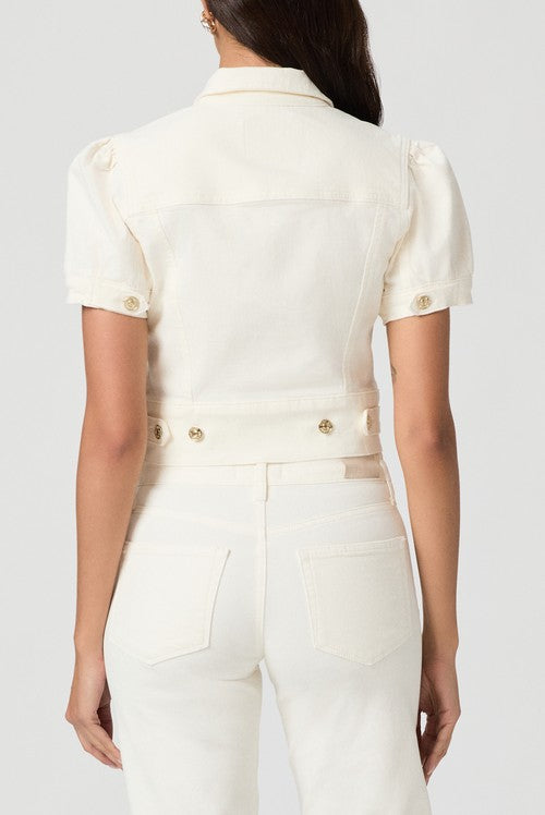 A woman with dark hair is seen from the back wearing the Paige Kendra Denim Jacket in Ecru, featuring short sleeves, gold buttons, double chest pockets, and matching high-waisted pants with a wide waistband against a light gray background.