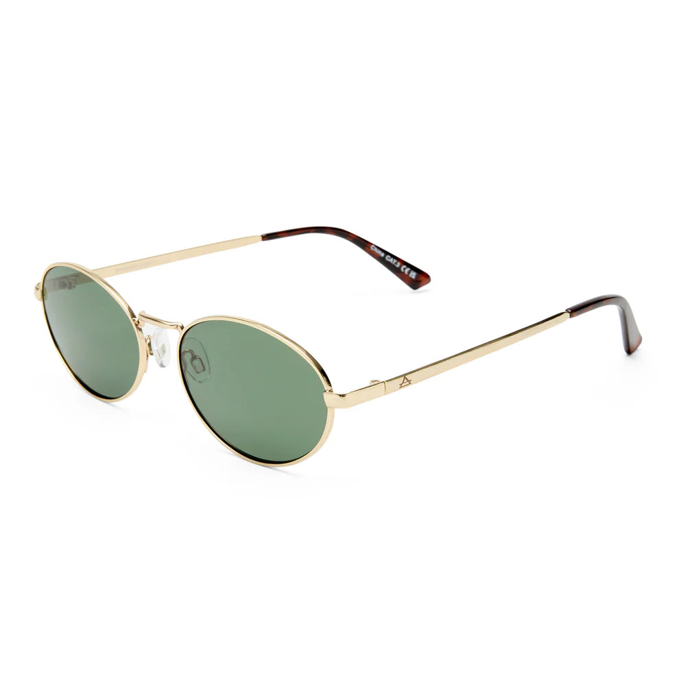 The Aire Ephermeris Sunnies feature gold frames, green-tinted scratch-resistant lenses, and thin arms with dark tips, all crafted from recycled metal and shown on a white background.