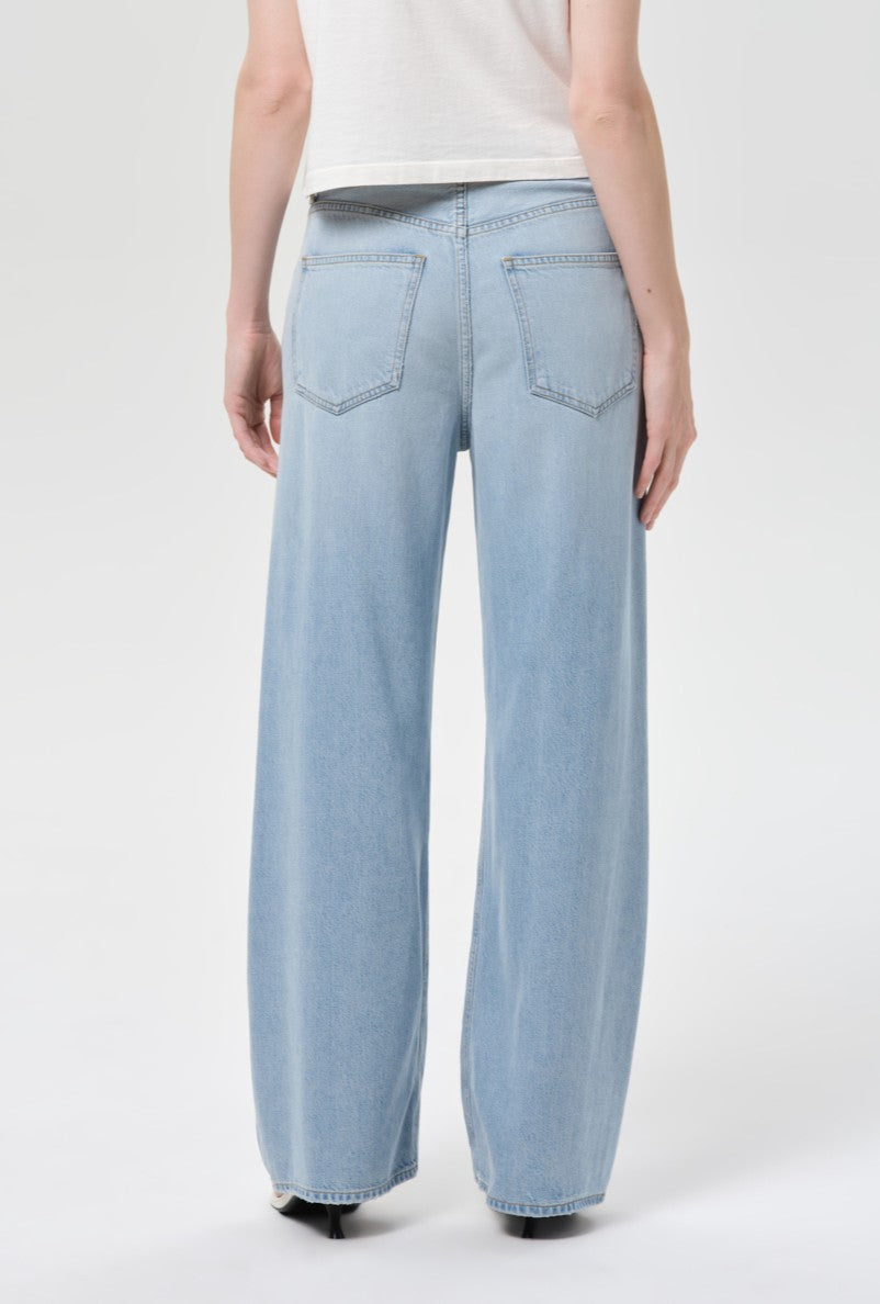 A person is shown from the back against a plain light background wearing AGOLDE’s Low Curve Jean In Memory, a full-length, light pale indigo denim pant crafted from breathable cotton, paired with a white shirt.
