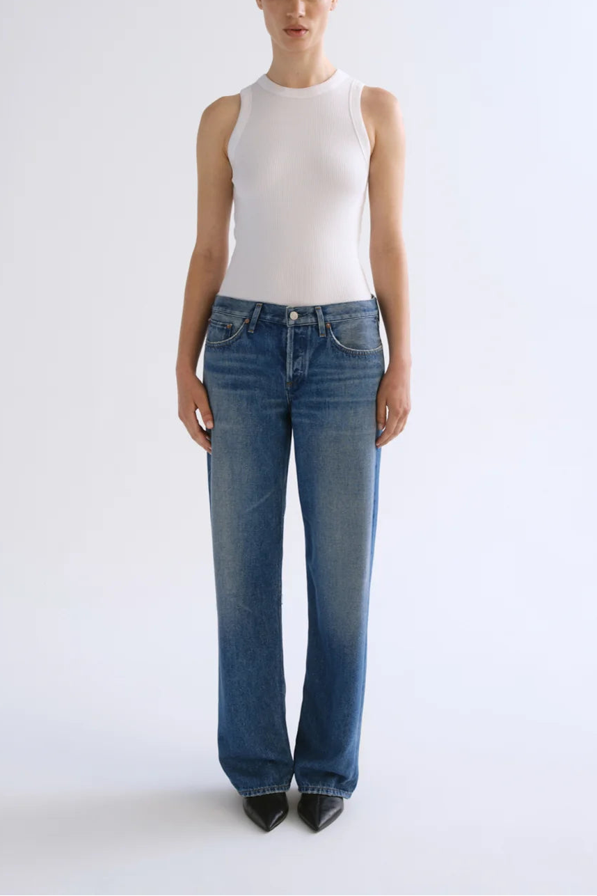 Person wearing white sleeveless ribbed tank top and low-rise medium-wash denim jeans with black pointed-toe heels.
