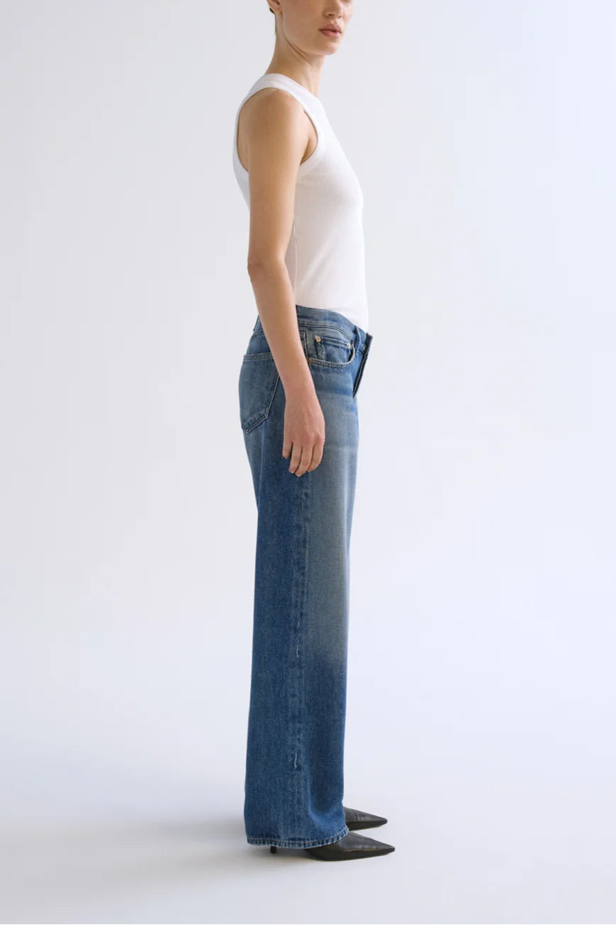Model wearing white sleeveless tank top and low-rise medium-wash blue jeans with straight leg silhouette.
