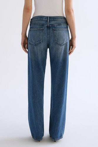 A person is shown from the back, standing against a plain light background, wearing a white top and AGOLDE's Low Rise Loose In Expression indigo denim pants.