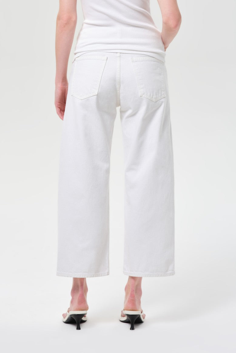 A person is shown from the back against a plain light background, wearing a white sleeveless top, AGOLDE Arc Jean 29 Inseam in Chalk White, and white heeled sandals.