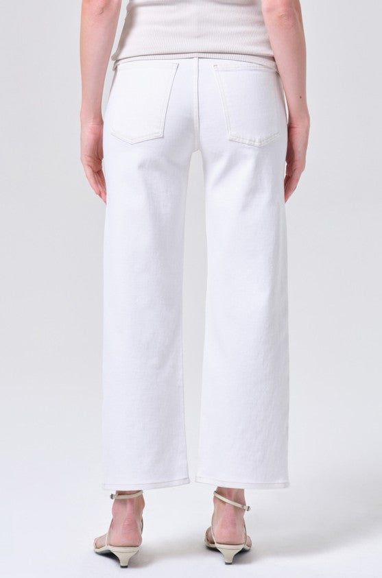 A person wearing the AGOLDE Harper Crop in White Wash, high-waisted wide-leg denim pants, and white heeled sandals stands facing away from the camera against a plain light background.