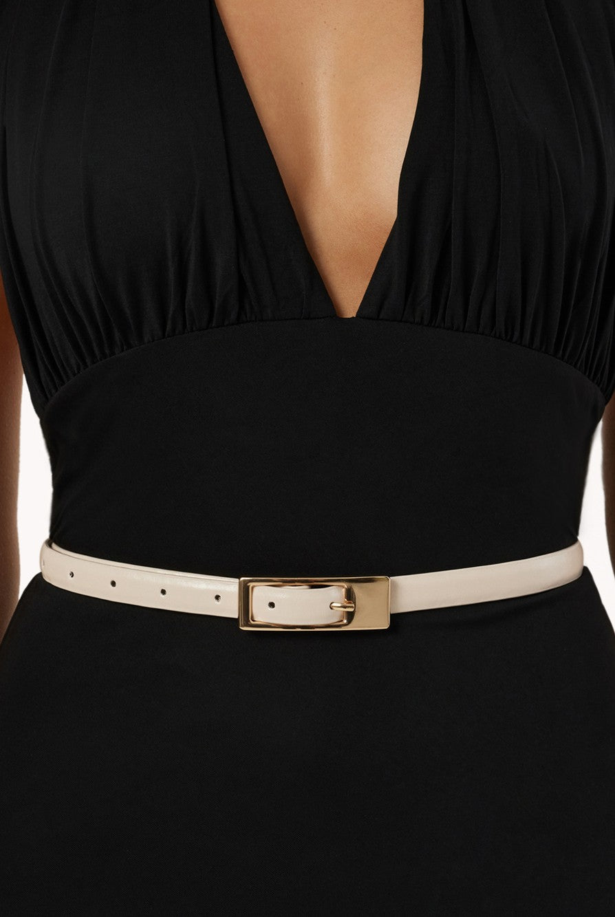 A person wearing a deep V-neck black dress with a fitted waist, accessorized with the Billini Gloria Thin Belt, a minimalist belt featuring a gold rectangular buckle.
