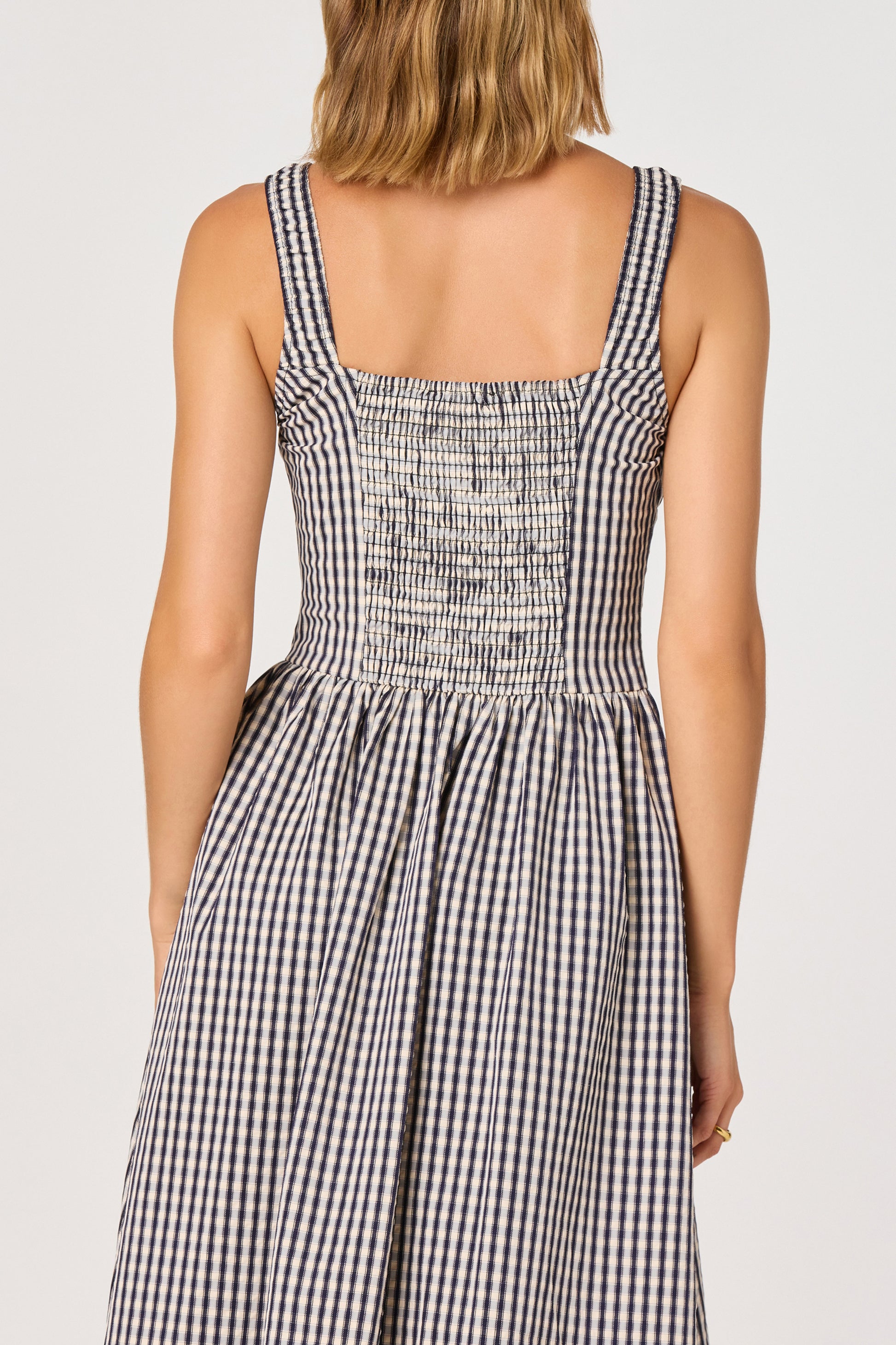 A woman shown from the back wearing the Temperance Maxi Dress by ASTR, a sleeveless woven maxi dress featuring a black and white gingham pattern, smocked tank straps, a shirred elasticized bodice, and a flared skirt.