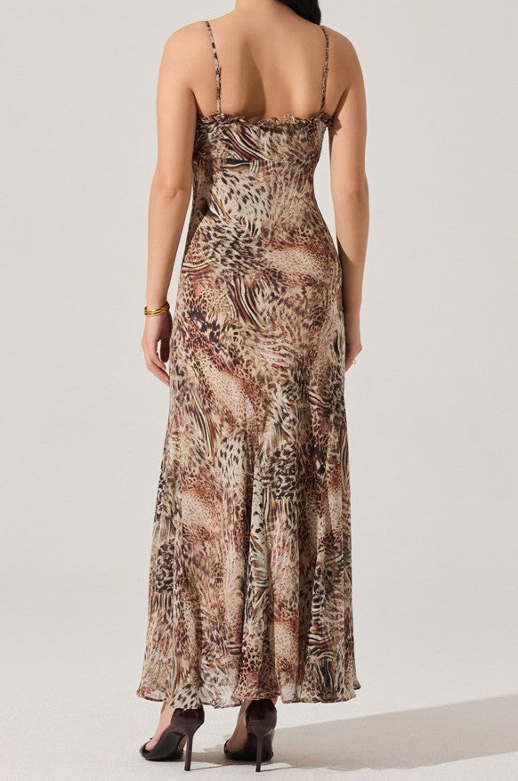 A woman faces away, wearing the Maeryn Maxi Dress by ASTR—a sleeveless animal print dress with a flowing silhouette. She pairs it with dark heels and a gold bracelet, her hair cascading down in effortless elegance.