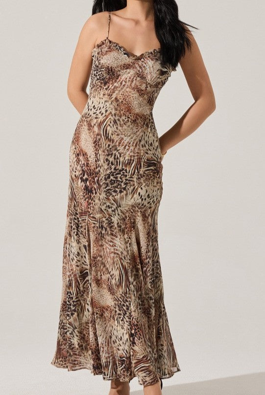 A woman radiates effortless elegance in the ASTR Maeryn Maxi Dress—a sleeveless, fitted animal-print style with thin straps and a flowing silhouette—as she stands against a plain light background, hands on hips and head turned slightly.