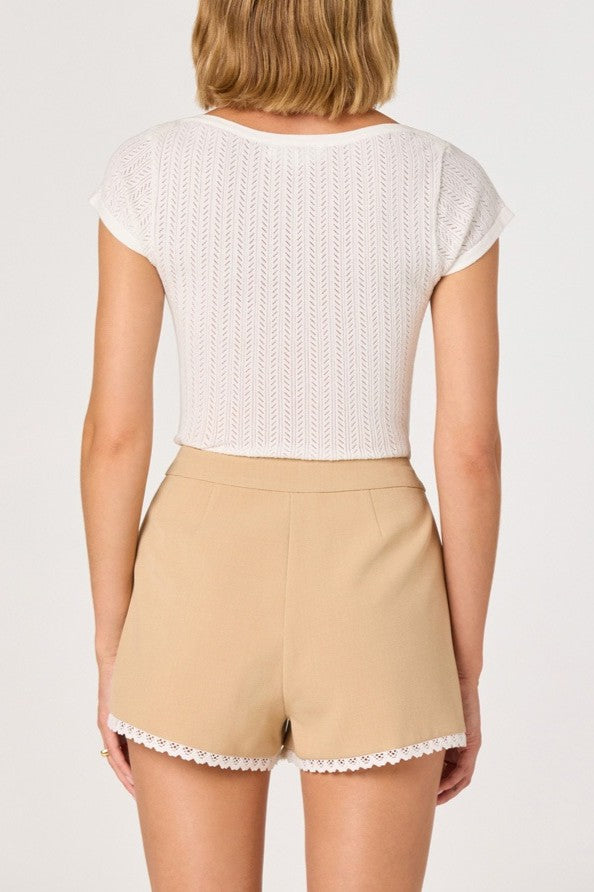 A woman is seen from the back wearing the ASTR River Short Sleeve Top with high-waisted beige shorts featuring lace trim at the hem, standing against a plain background.