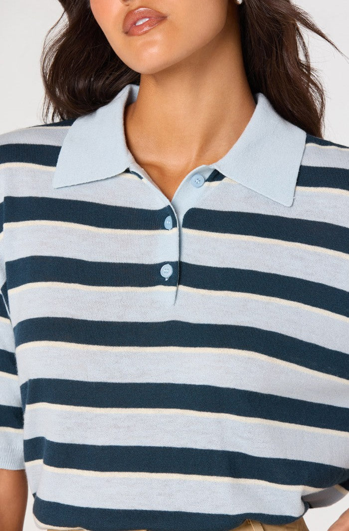 A woman wearing the ASTR Scottie Sweater—a collared, short-sleeved lightweight knit polo featuring blue, white, and beige horizontal stripes. The shirt has a ribbed collar and a relaxed fit silhouette. Only her lower face and upper torso are visible.