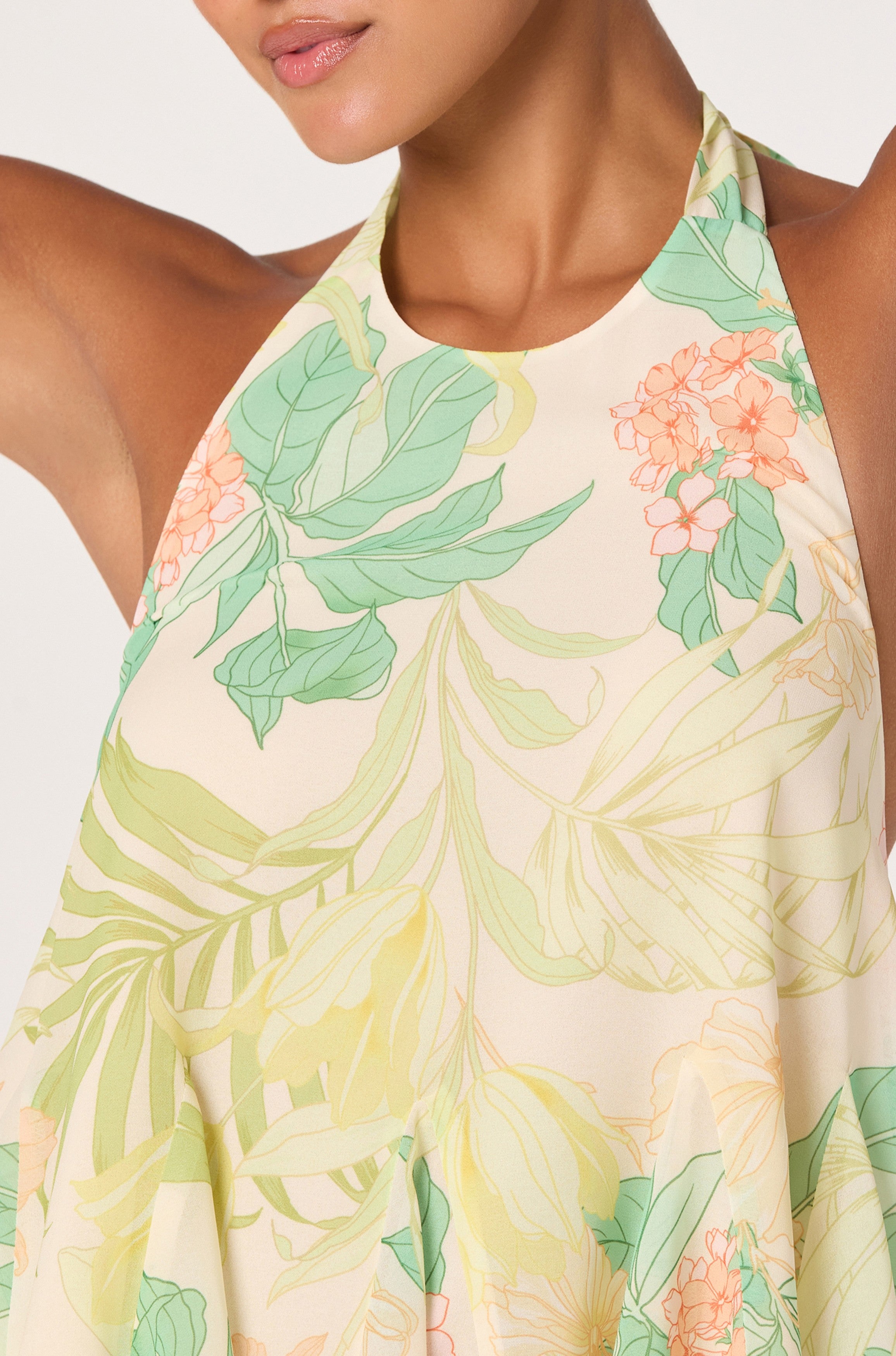 A woman models the ASTR Belen Top, a chiffon babydoll halter with a pastel floral and leaf print in green, yellow, and peach. The photo is cropped to show her upper body and part of her face.