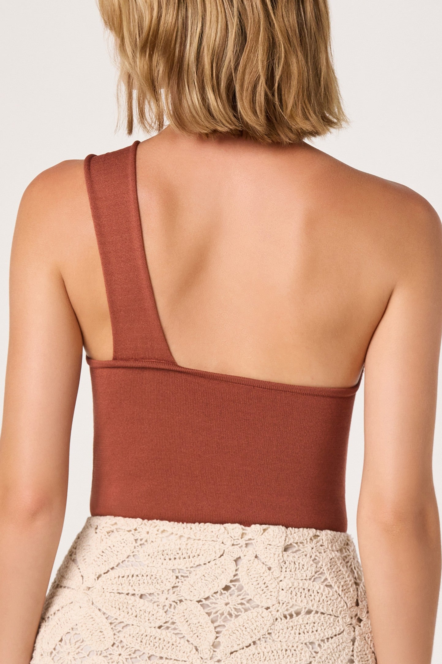 A person with short, light brown hair is seen from behind in a slim fit, rust Ania Top by ASTR and a cream crochet skirt against a plain light background.