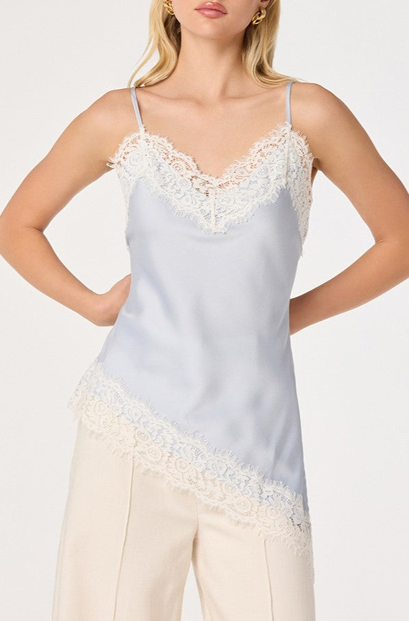 A woman wears the ASTR Analise Top, a light blue satin tank featuring eyelash lace trim at the neckline and hem, paired with cream-colored pants. The background is plain white.