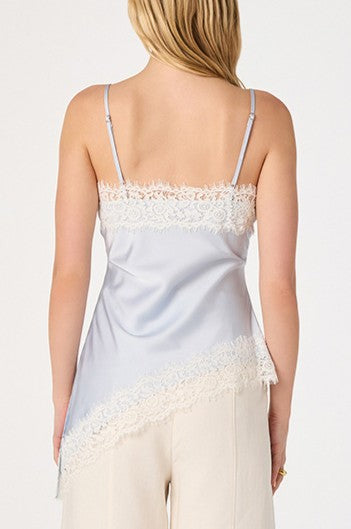 A woman with blonde hair stands against a plain background wearing the ASTR Analise Top, a silky satin tank featuring eyelash lace trim at the neckline and hem, paired with light-colored pants.