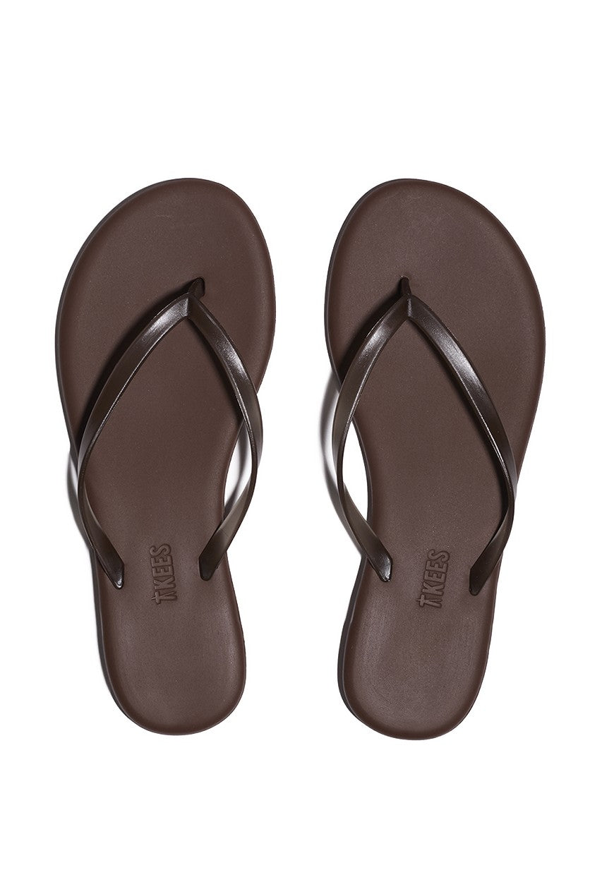 The Aqua Tkees In Brun by Tkees are brown flip-flop sandals with thin leather straps, shown side by side from above on a white background.