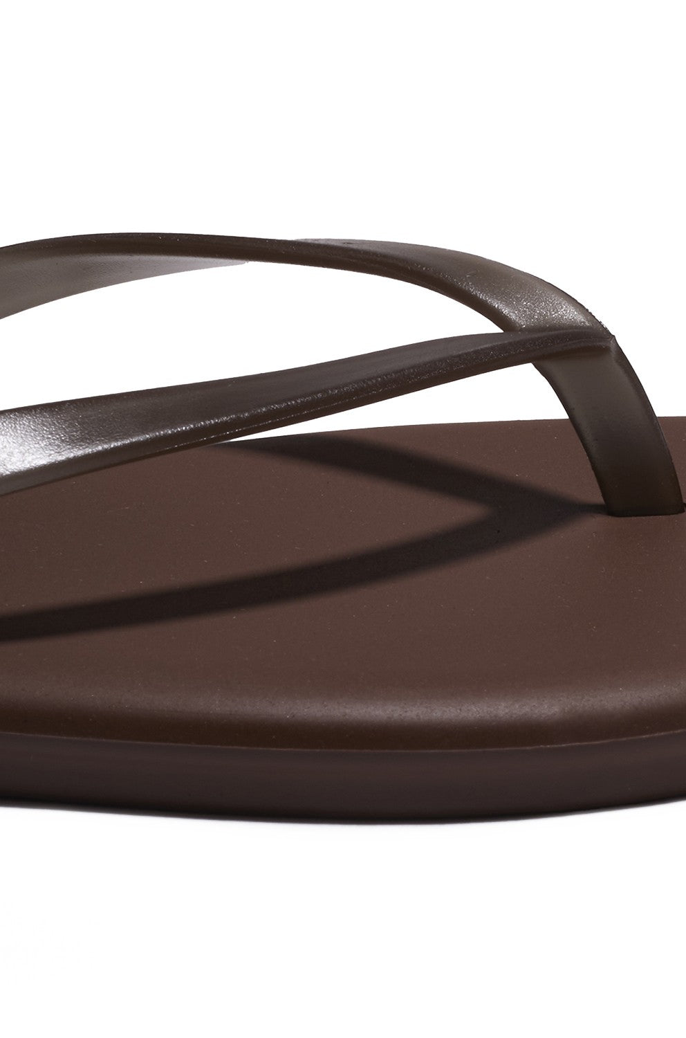 Close-up of the Aqua Tkees In Brun flip-flop by Tkees, featuring a brown leather upper, toe strap, and cushioned footbed, displayed against a white background.