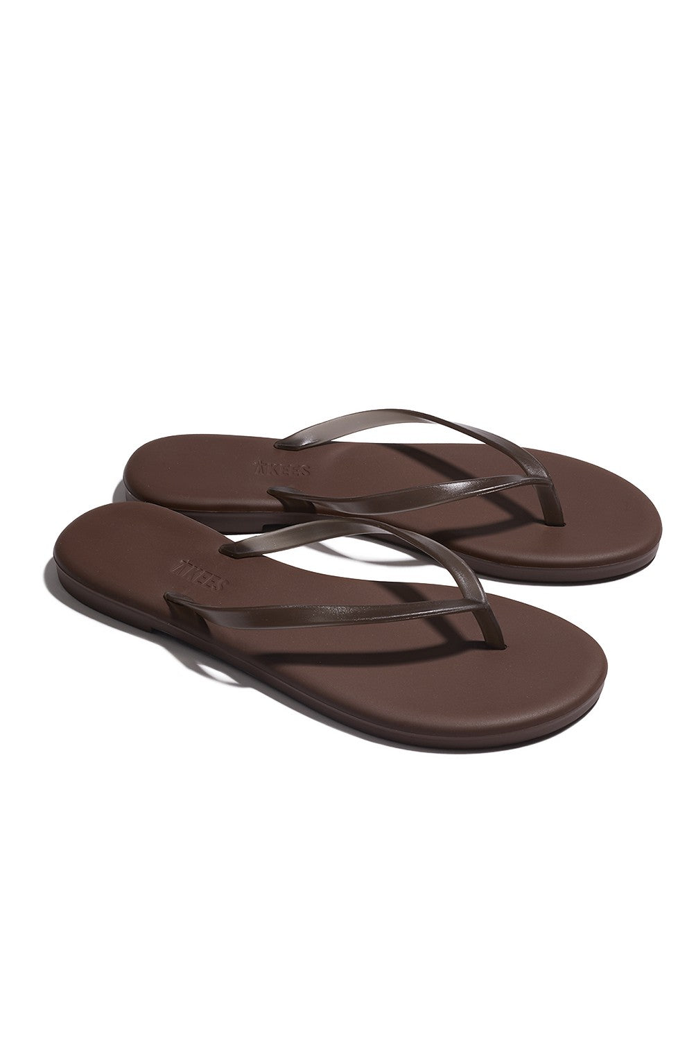 Aqua Tkees In Brun by Tkees are simple brown flip-flop sandals with thin straps, flat soles, and a cushioned footbed, shown against a white background.