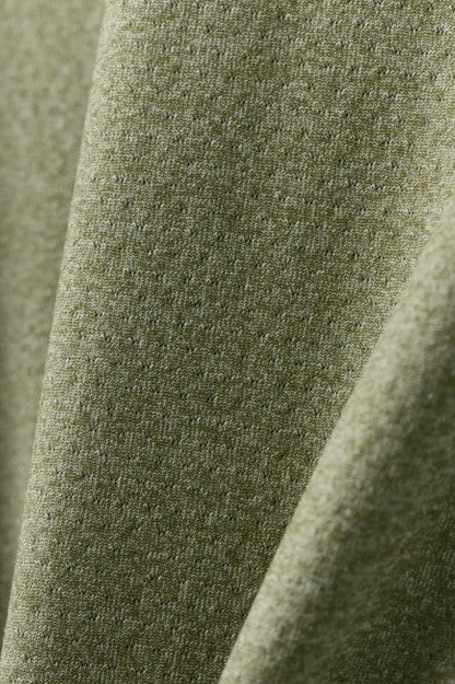 Close-up of the RHONE Atmosphere Tee’s lightweight performance fabric in light olive green, showcasing a subtle dotted texture with gentle folds and soft shadows.