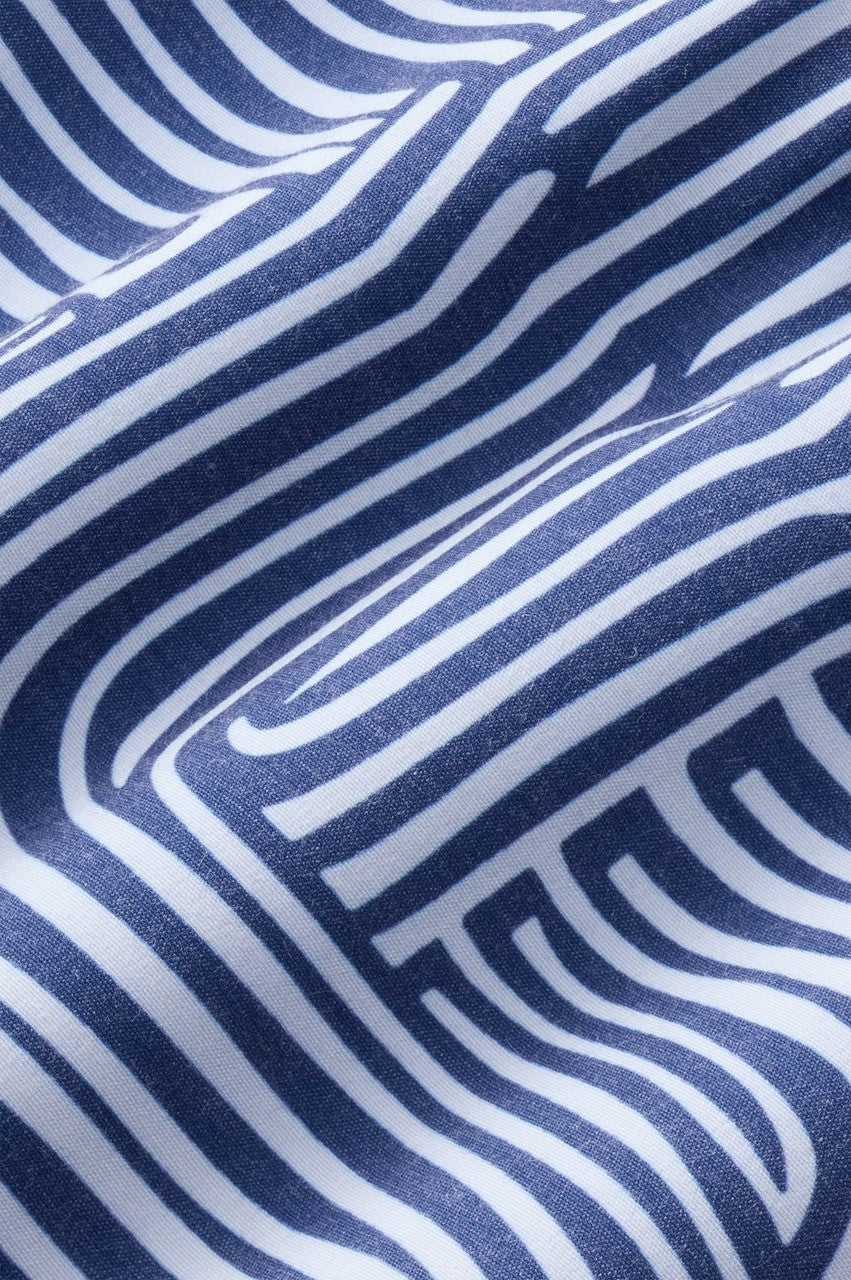 A close-up of the Bayberry Trunk 7 Inch Wavy Sands by Fair Harbor, made from white recycled polyester featuring bold navy geometric lines in a maze-like pattern. The fabric is slightly wrinkled, adding gentle shadows and texture.