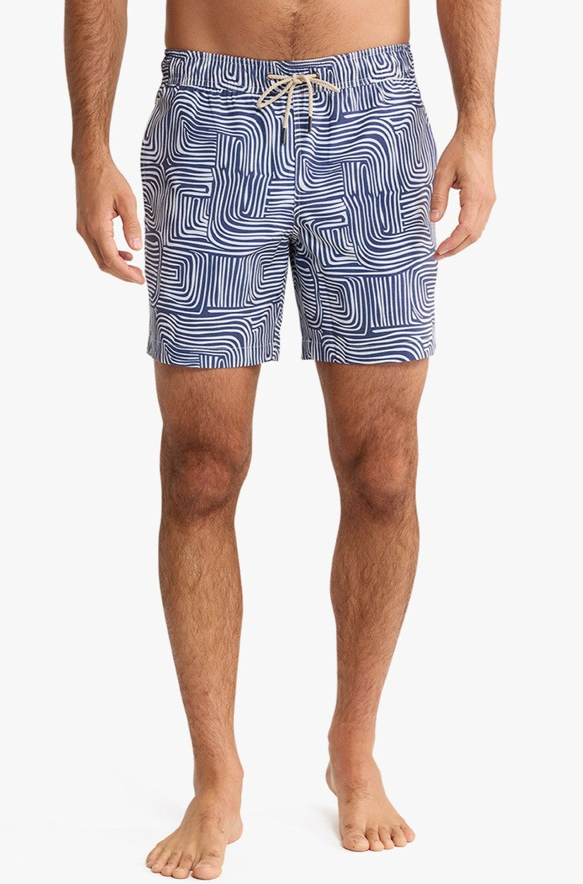 A person stands barefoot, shown from the waist down against a plain background, wearing Fair Harbor’s Bayberry Trunk 7 Inch Wavy Sands swim trunks in Navy Multi.