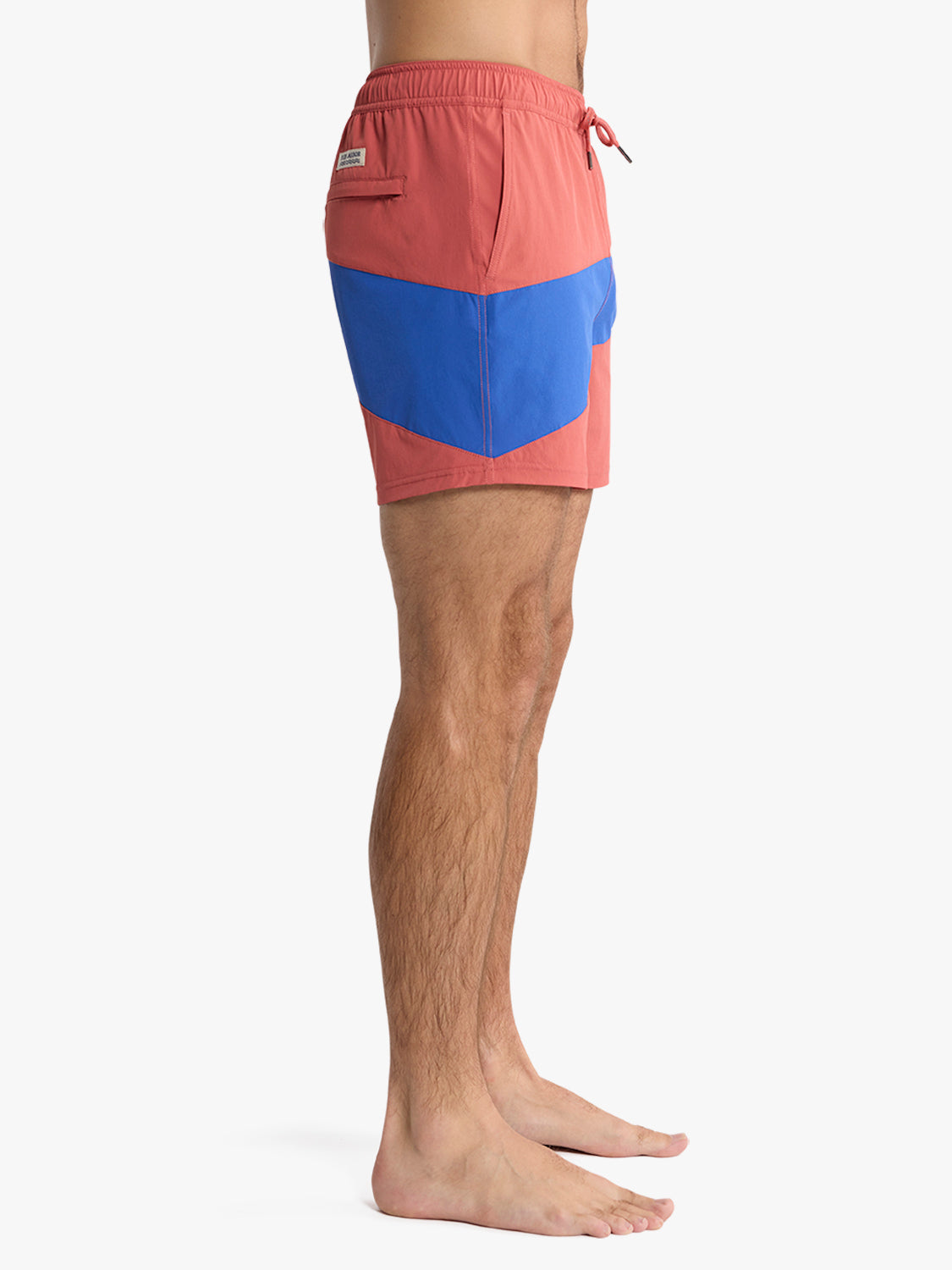 A person stands barefoot in profile against a white background, wearing Fair Harbor's Bungalow Trunk 5" in Nautical Colorblock—recycled nylon shorts with a quick-dry finish, drawstring waistband, and back pocket.