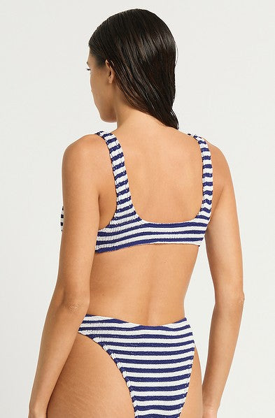 A woman with wet, dark hair is shown from the back wearing the Bond-Eye Navy White Scout Crop, a blue and white striped bikini top offering medium to full support—ideal for larger busts—against a plain, light background.