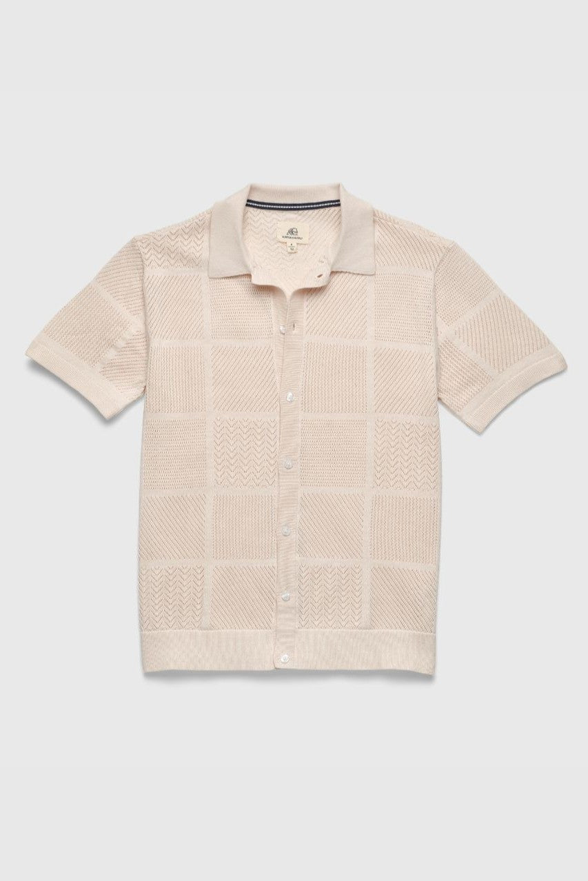 The Brent Open Stitch Button Front Sweater by Surfside Supply Co. is a beige, short-sleeve, collared 100% cotton sweater with a textured checkered pattern, ribbed hems, and buttons up the front. Shown laid flat on a light background.