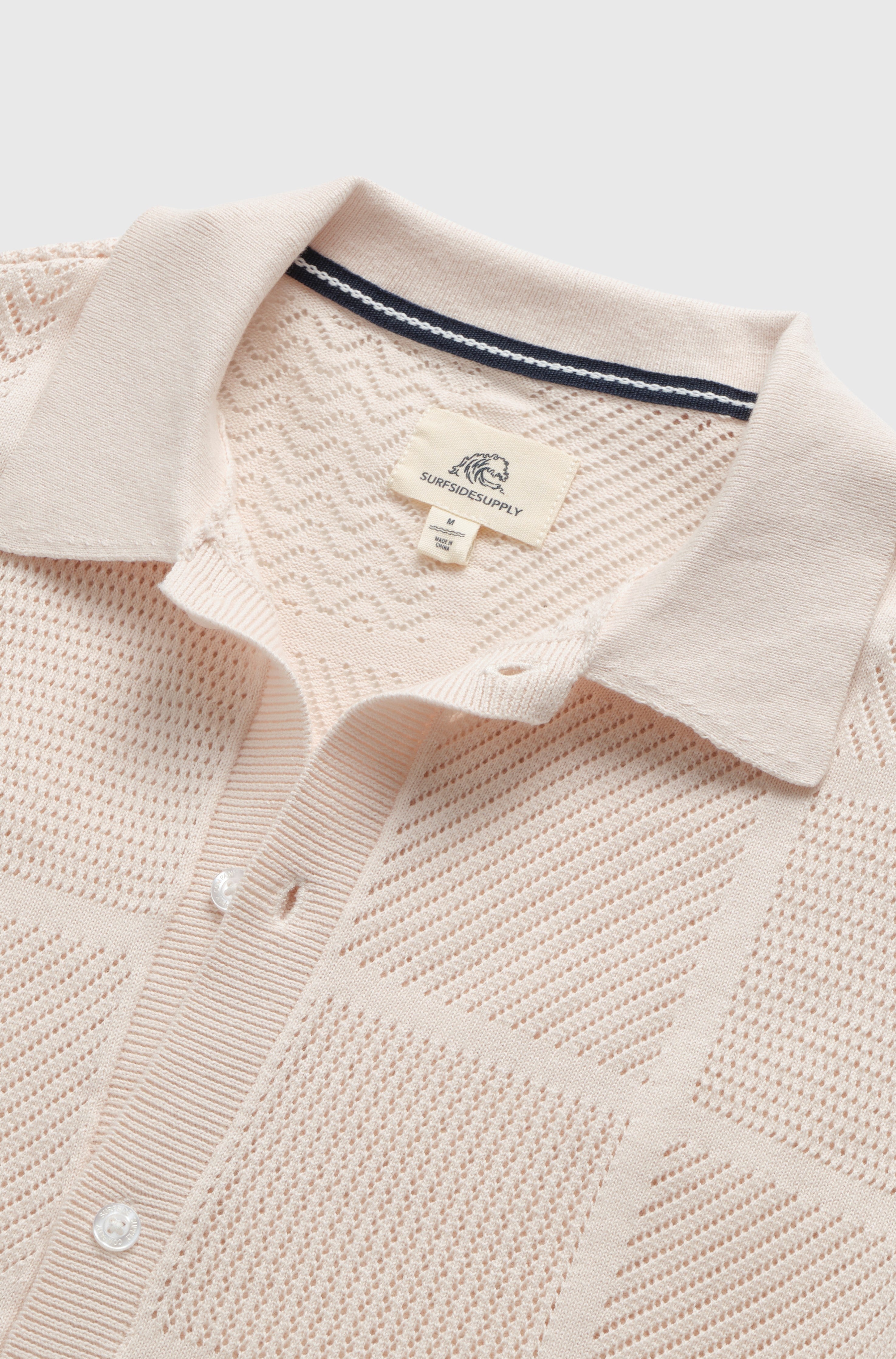 A close-up of an off white Brent Open Stitch Button Front Sweater by Surfside Supply Co., featuring 100% cotton, short sleeves, a textured checkered pattern, a collar, white buttons, and a label inside the neckline.