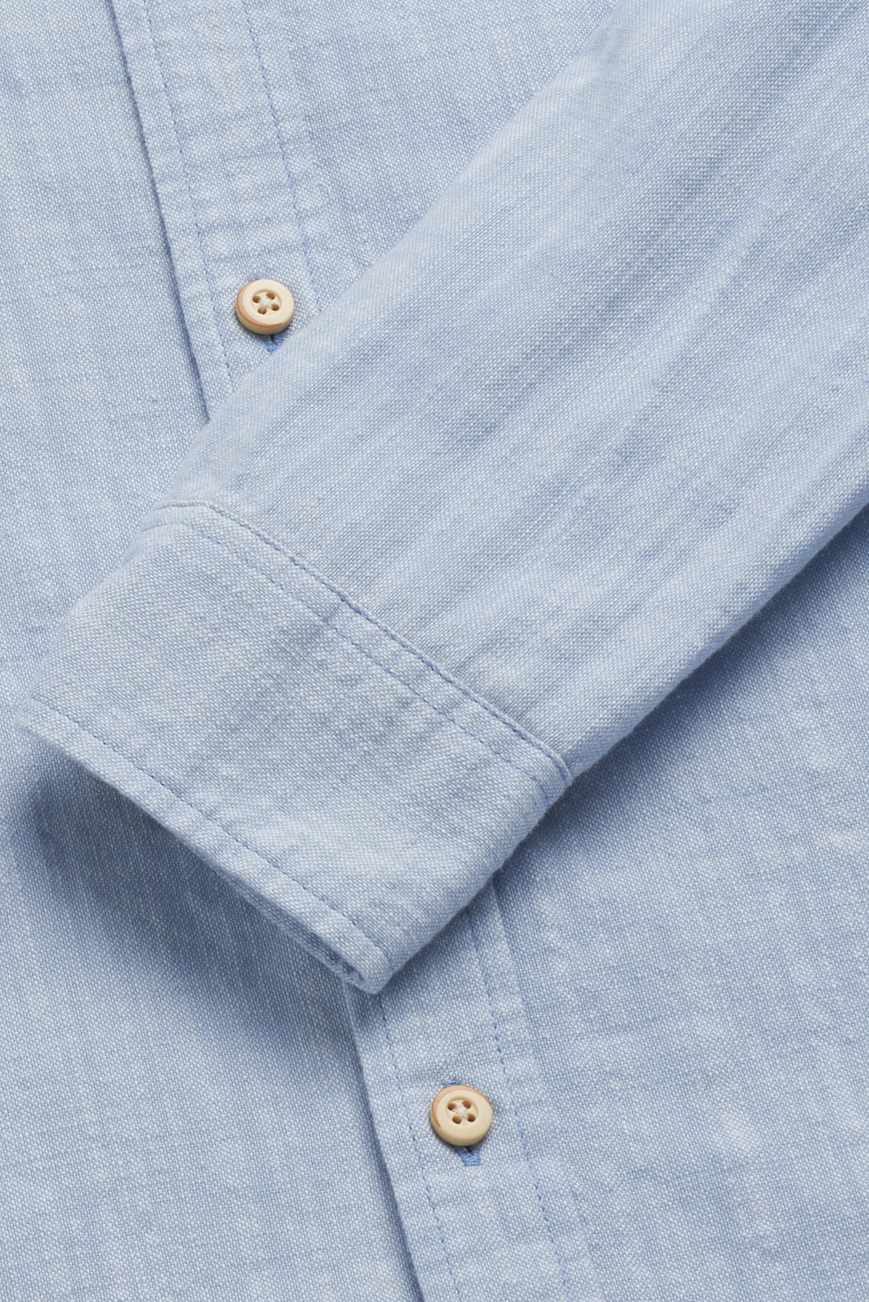 Close-up of the Brian Long Sleeve 2tone Slub Shirt by Surfside Supply Co., featuring light blue textured cotton, a sleeve cuff with two beige buttons, and a hint of a chest pocket for classic style detail.