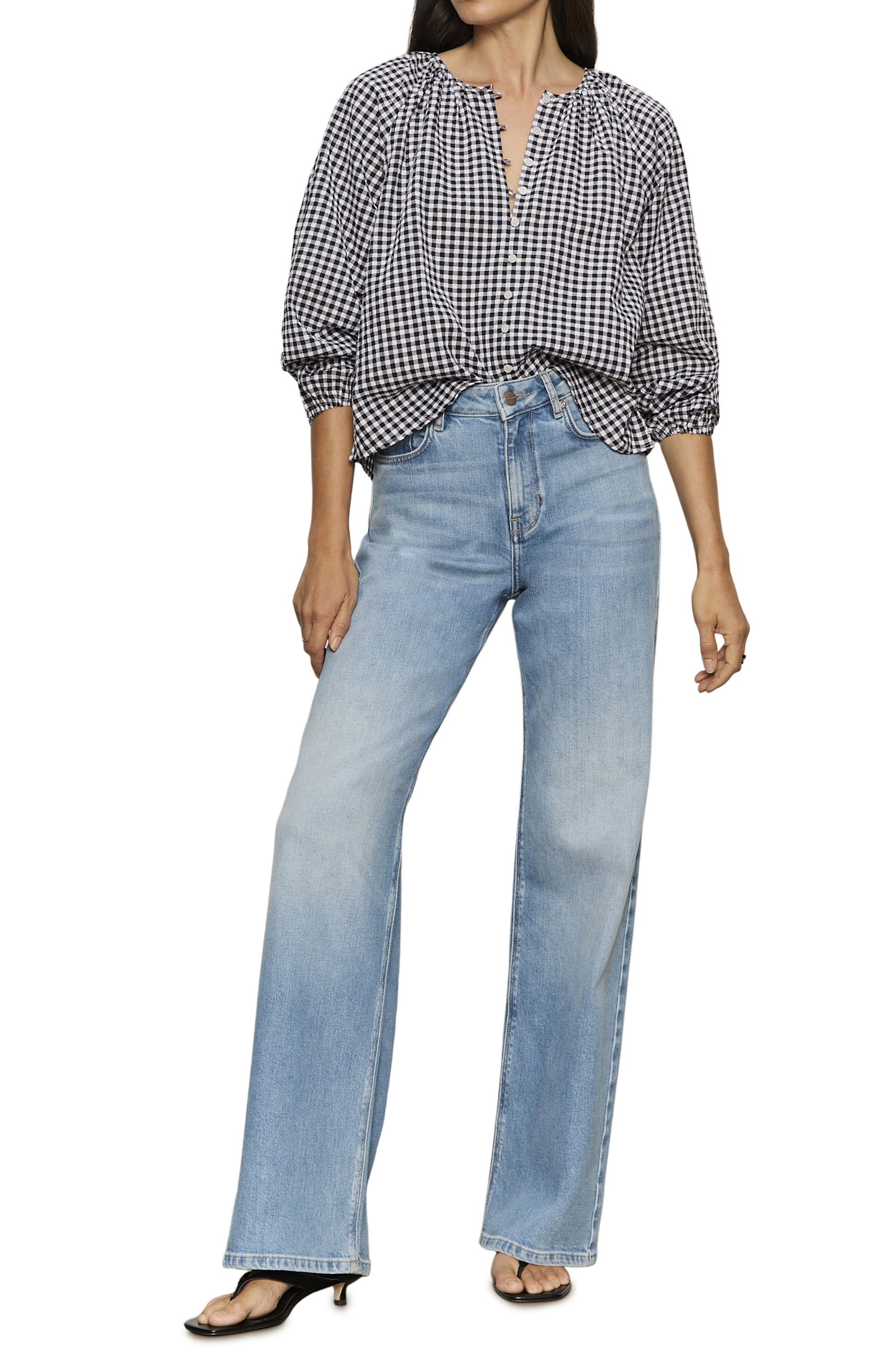 A person wearing Sanctuary's Perfect Gingham Button Blouse in black and white, paired with light blue high-waisted wide-leg jeans and black open-toe heeled sandals, standing against a white background.