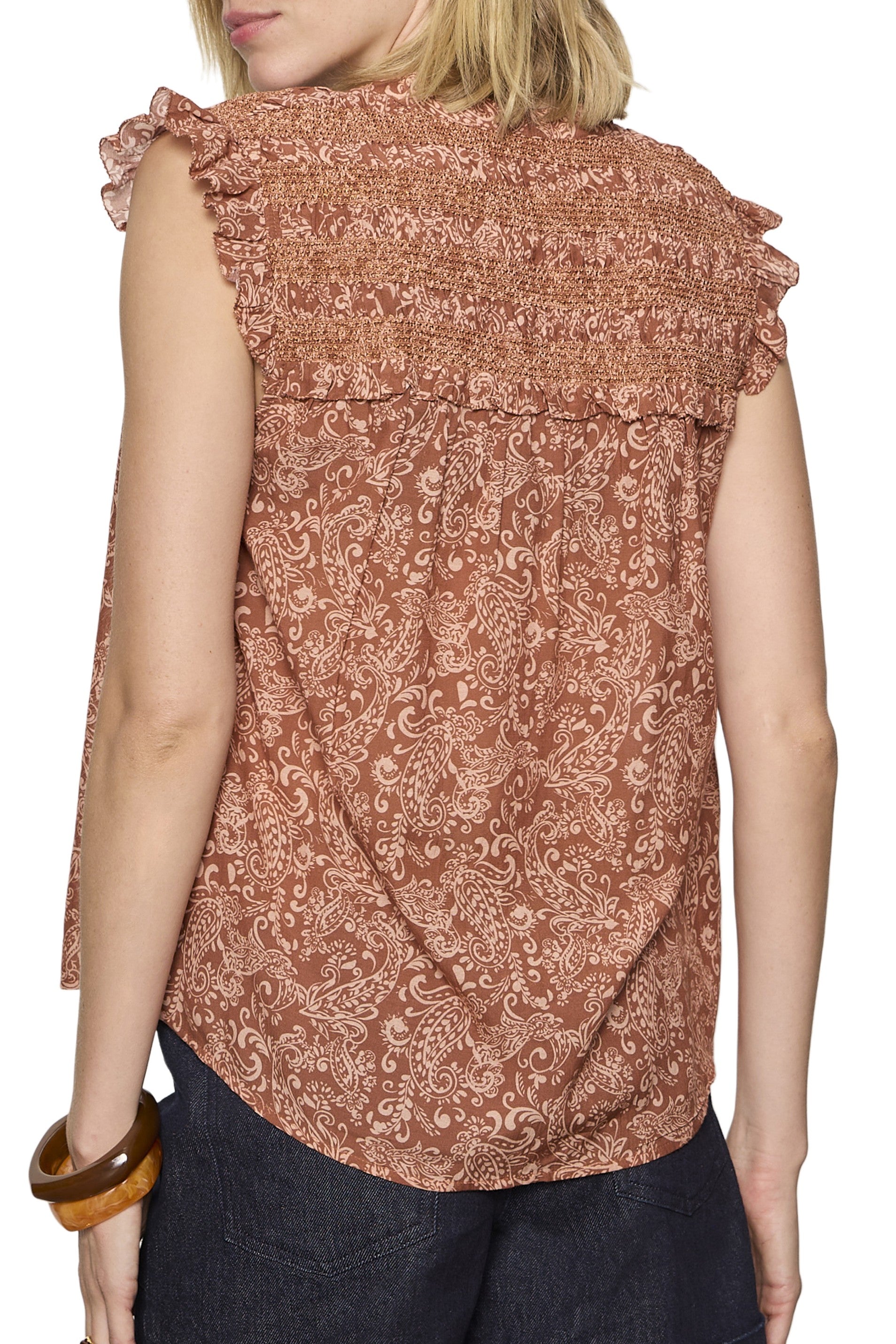 A person wears the Sanctuary Free Feeling Smocked Blouse—a sleeveless, rust paisley top with ruffled shoulders and smocked back—paired with dark pants and a large brown bangle.