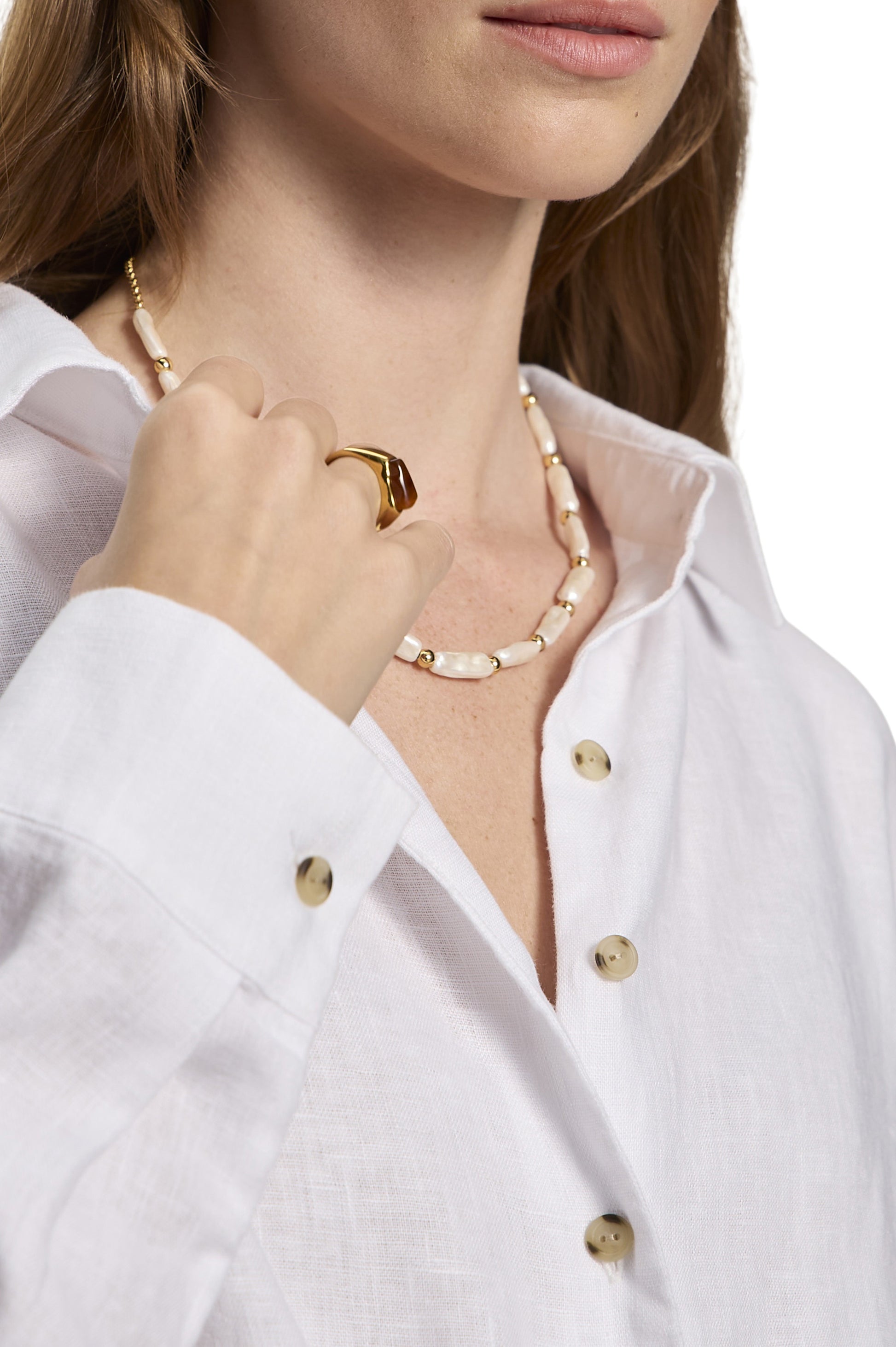 A woman wears the Sanctuary More Love Linen Tie Top in white, styled with a gold and pearl necklace and a gold ring. She is pictured from the shoulders up, her hand near her collar, against a plain white background.