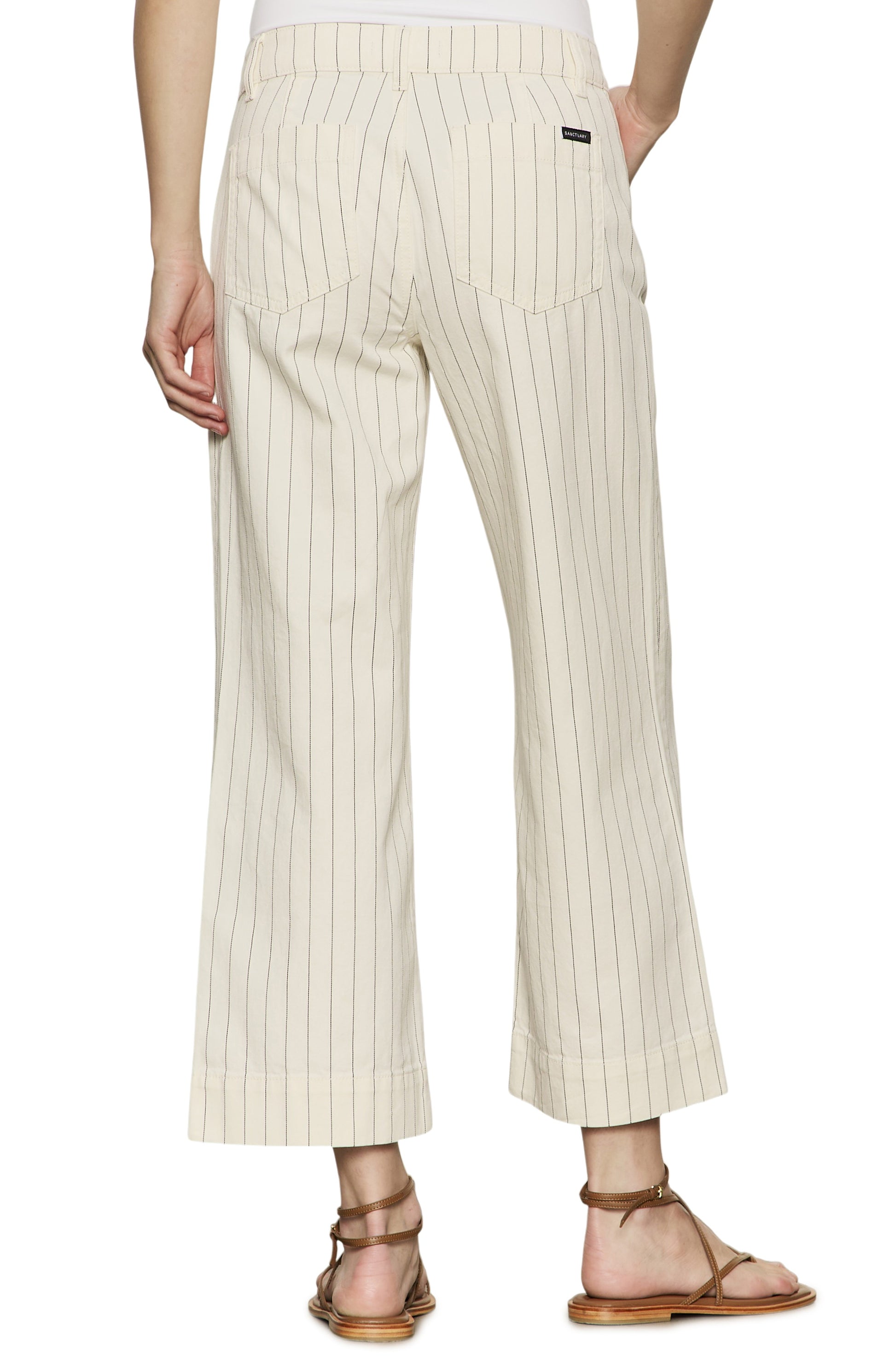 Wearing Sanctuary's The Marine Bleached White Pinstripe relaxed fit, cropped wide leg pants with back pockets and flat brown sandals. Photo taken from behind, highlighting the lower body in cream pinstripes.