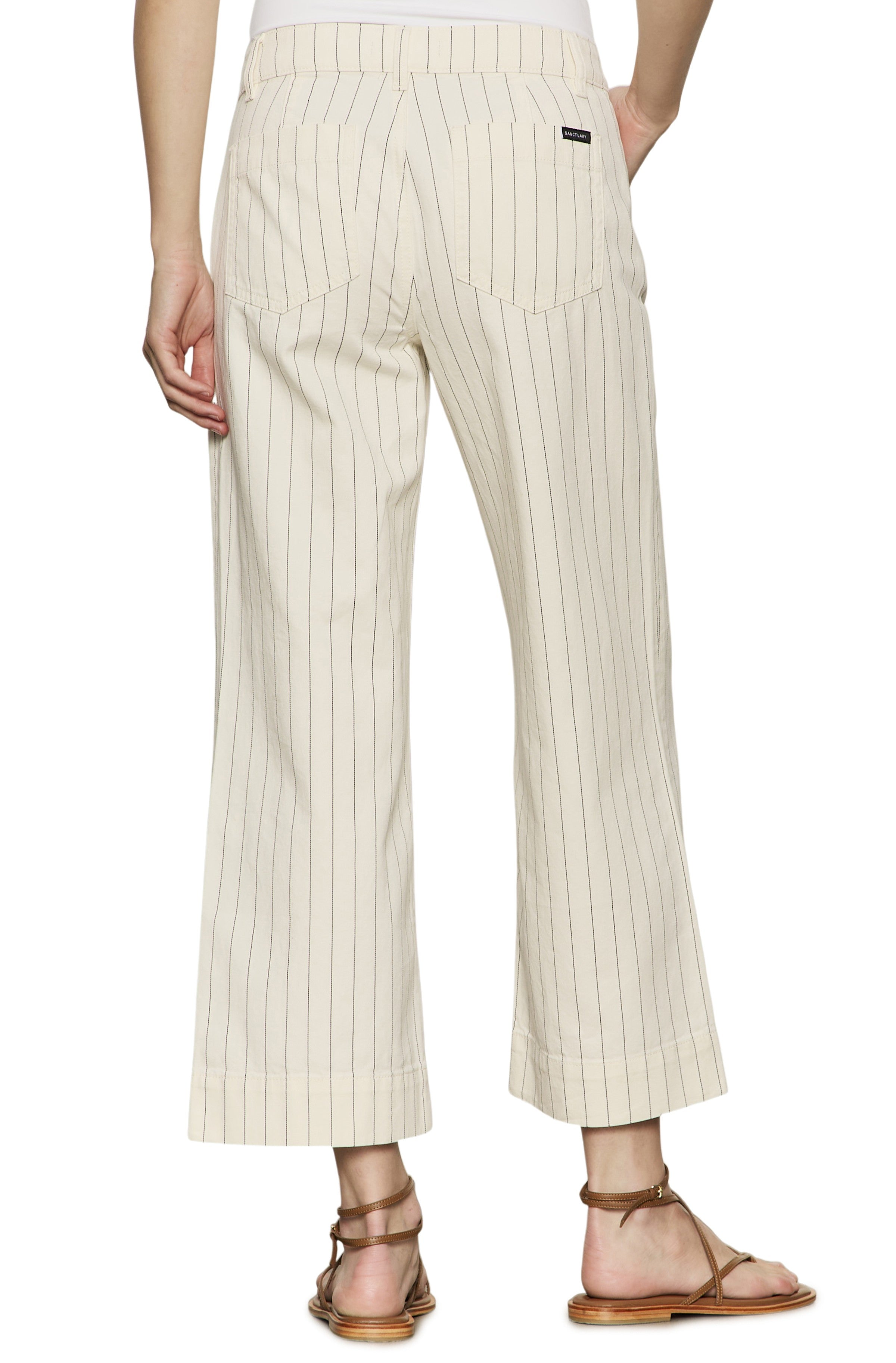 Wearing Sanctuary's The Marine Bleached White Pinstripe relaxed fit, cropped wide leg pants with back pockets and flat brown sandals. Photo taken from behind, highlighting the lower body in cream pinstripes.