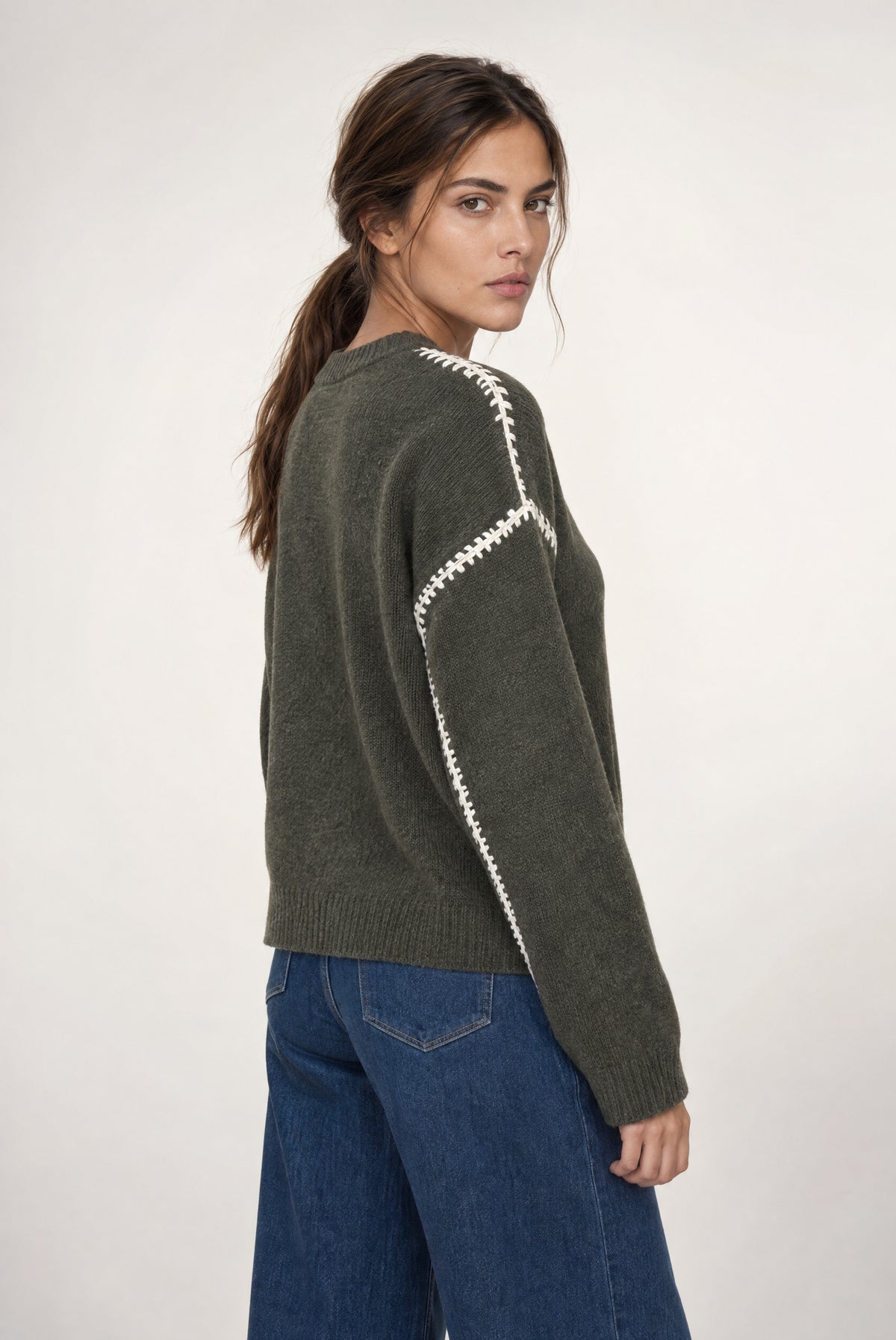 Olive sweater with ivory stitching detail on back, worn with dark blue jeans.