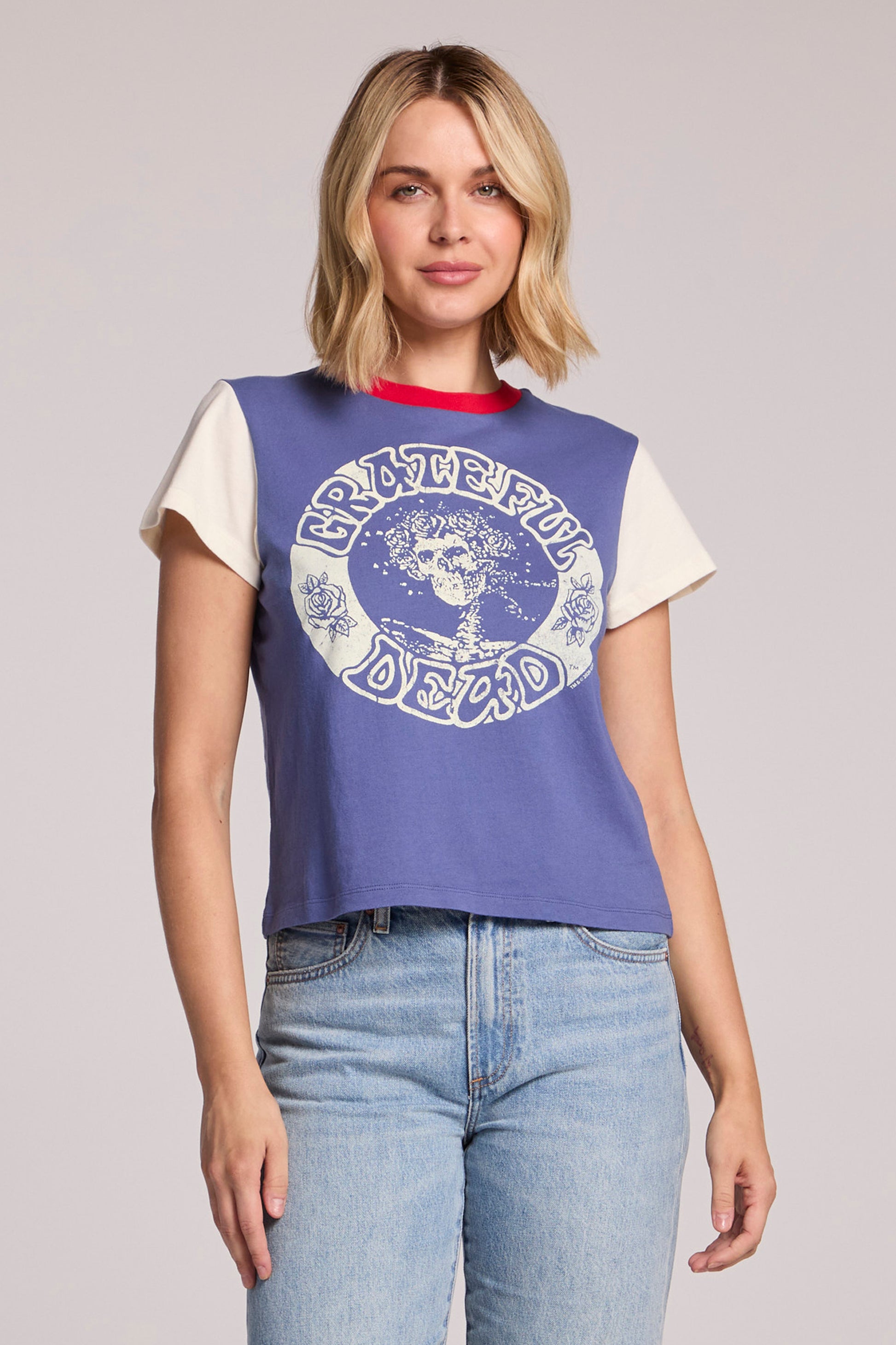 A woman with blonde hair wears the Chaser Grateful Dead - Classic Bertha tee in Blue Multi, featuring a Bertha skull graphic, and light blue jeans, standing against a neutral background.